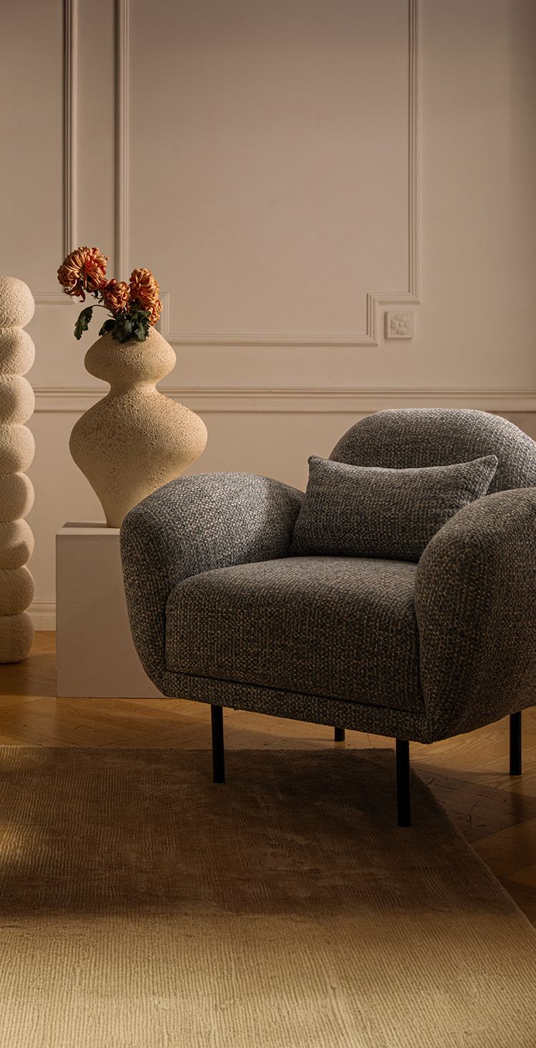 Lit Micadoni avec tête de lit capitonnée arrondie et fauteuil gris texturé dans une chambre chaleureuse.