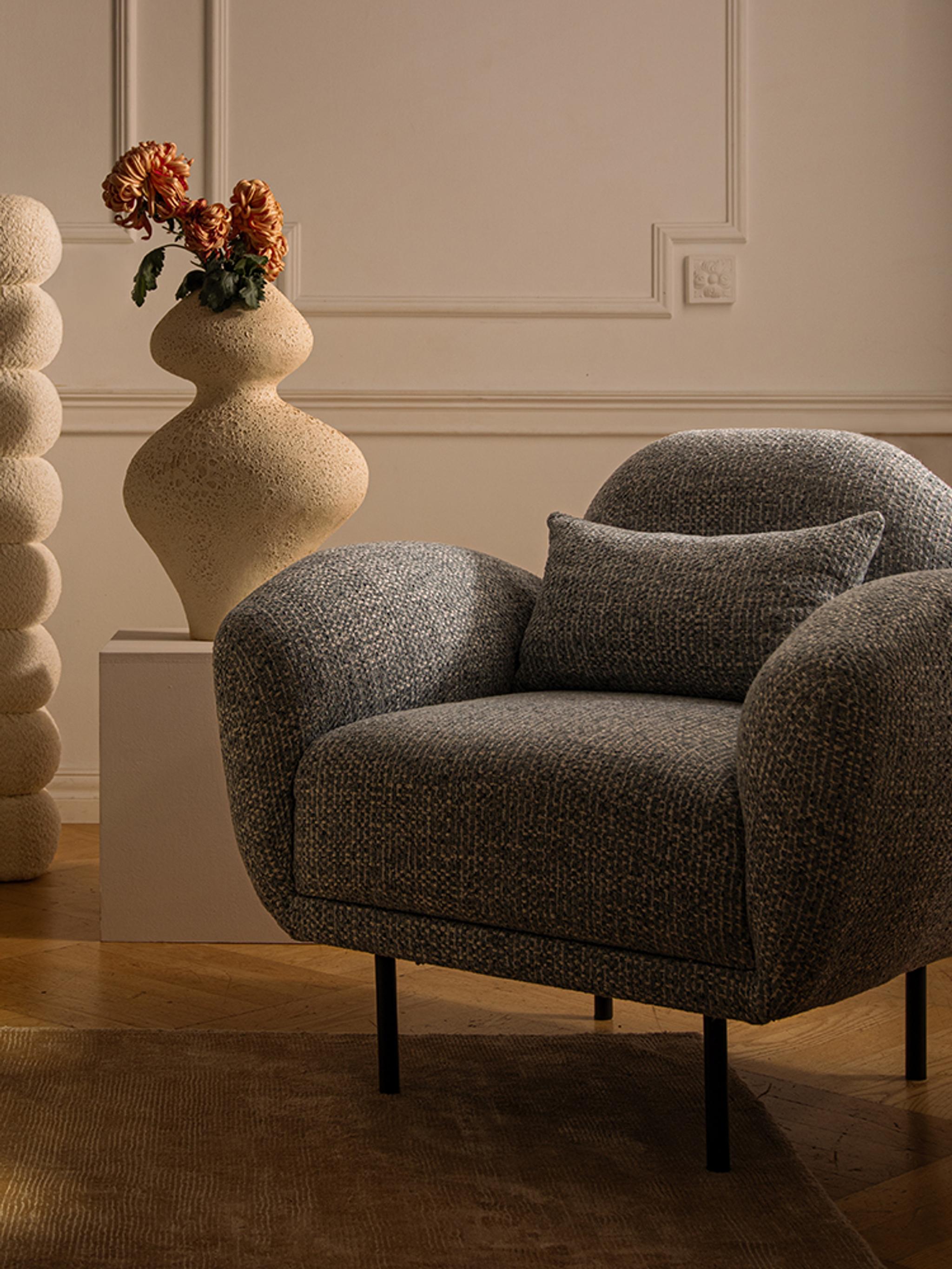 Lit Micadoni avec tête de lit capitonnée arrondie et fauteuil gris texturé dans une chambre chaleureuse.