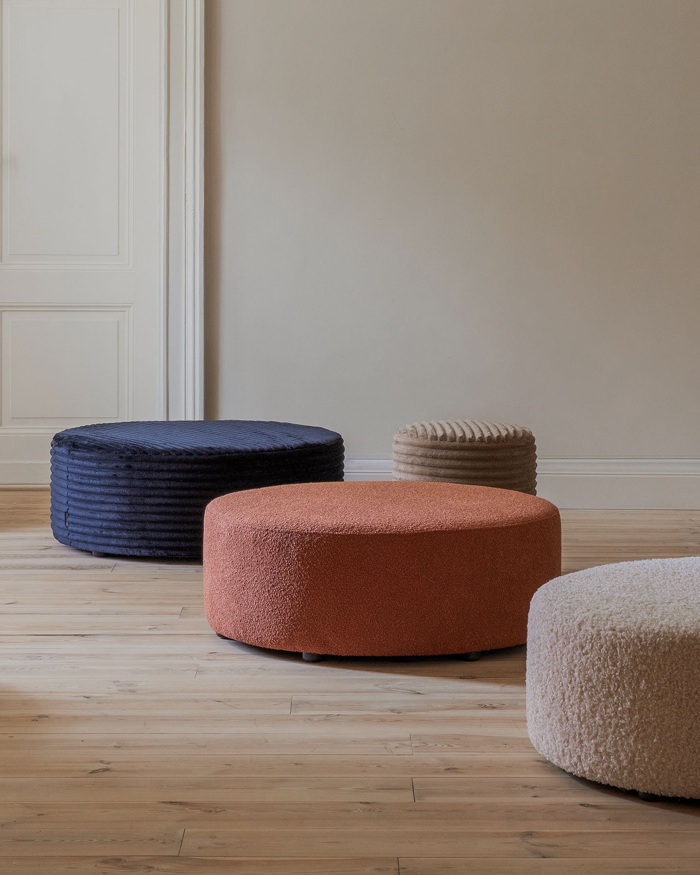 Page de la collection Micadoni AW25 avec canapé d’angle arrondi beige et table basse ronde en bois dans un intérieur chaleureux aux fenêtres cintrées.