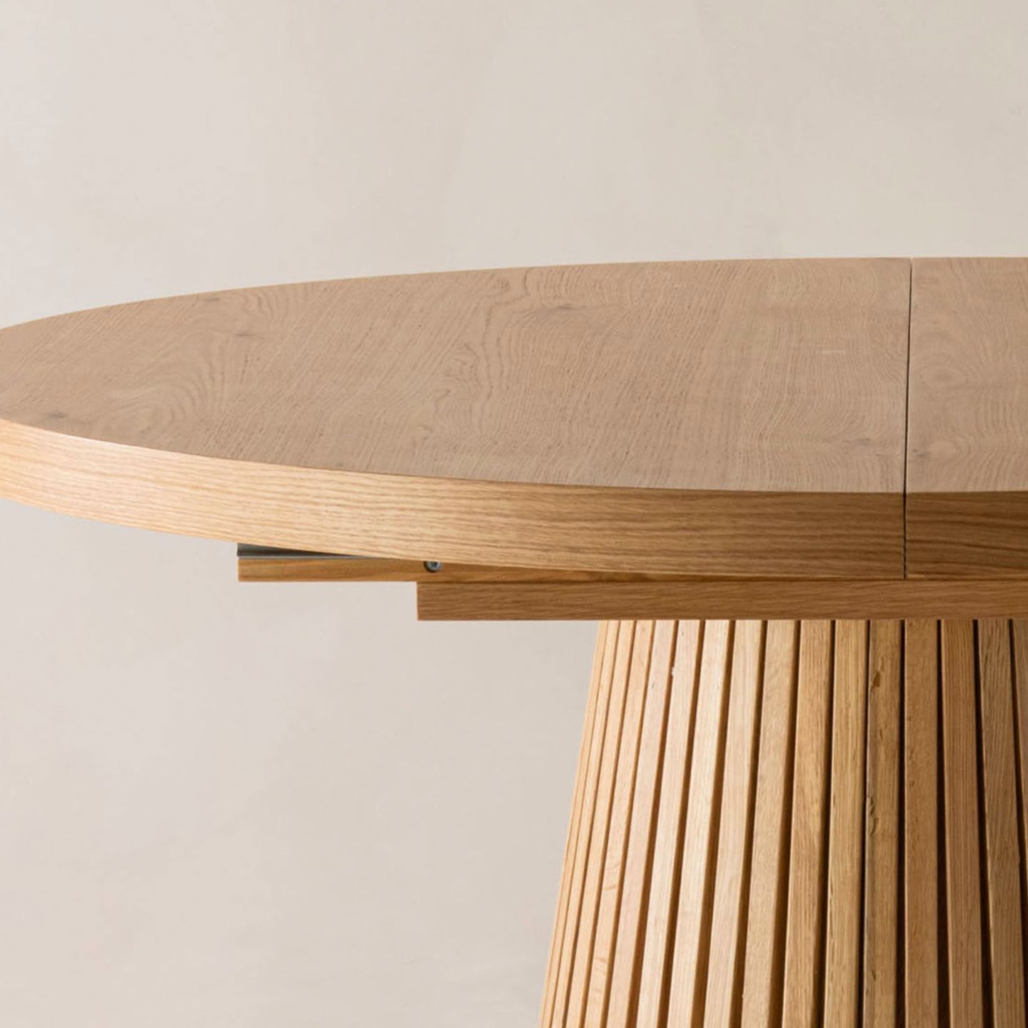 Gros plan d’une table de salle à manger Micadoni ronde et extensible en chêne, avec piètement cannelé et joint central visible.