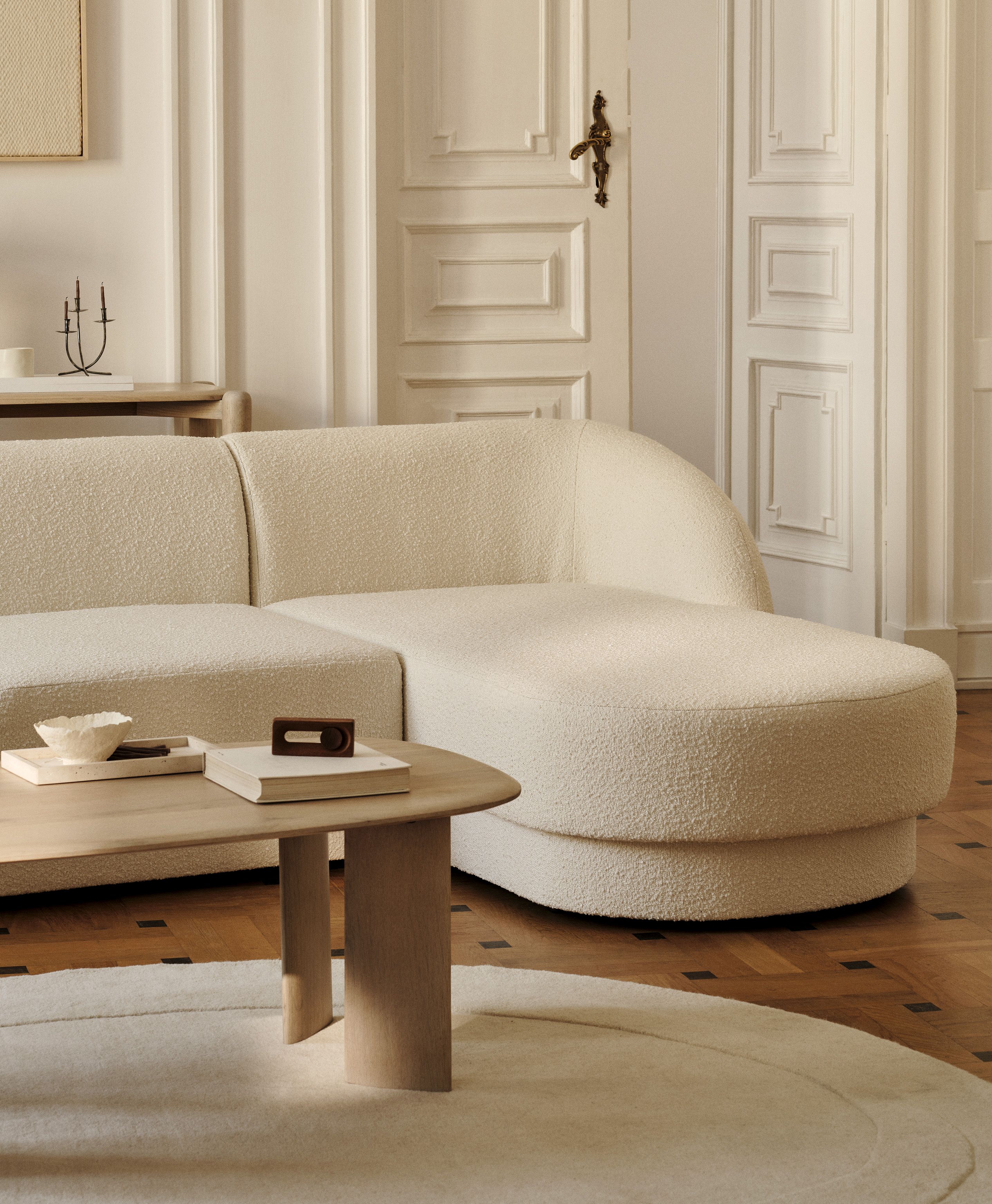 Canapé d’angle Miley en tissu bouclé crème aux bords arrondis, associé à une table basse ovale Aggie en bois – mobilier Micadoni