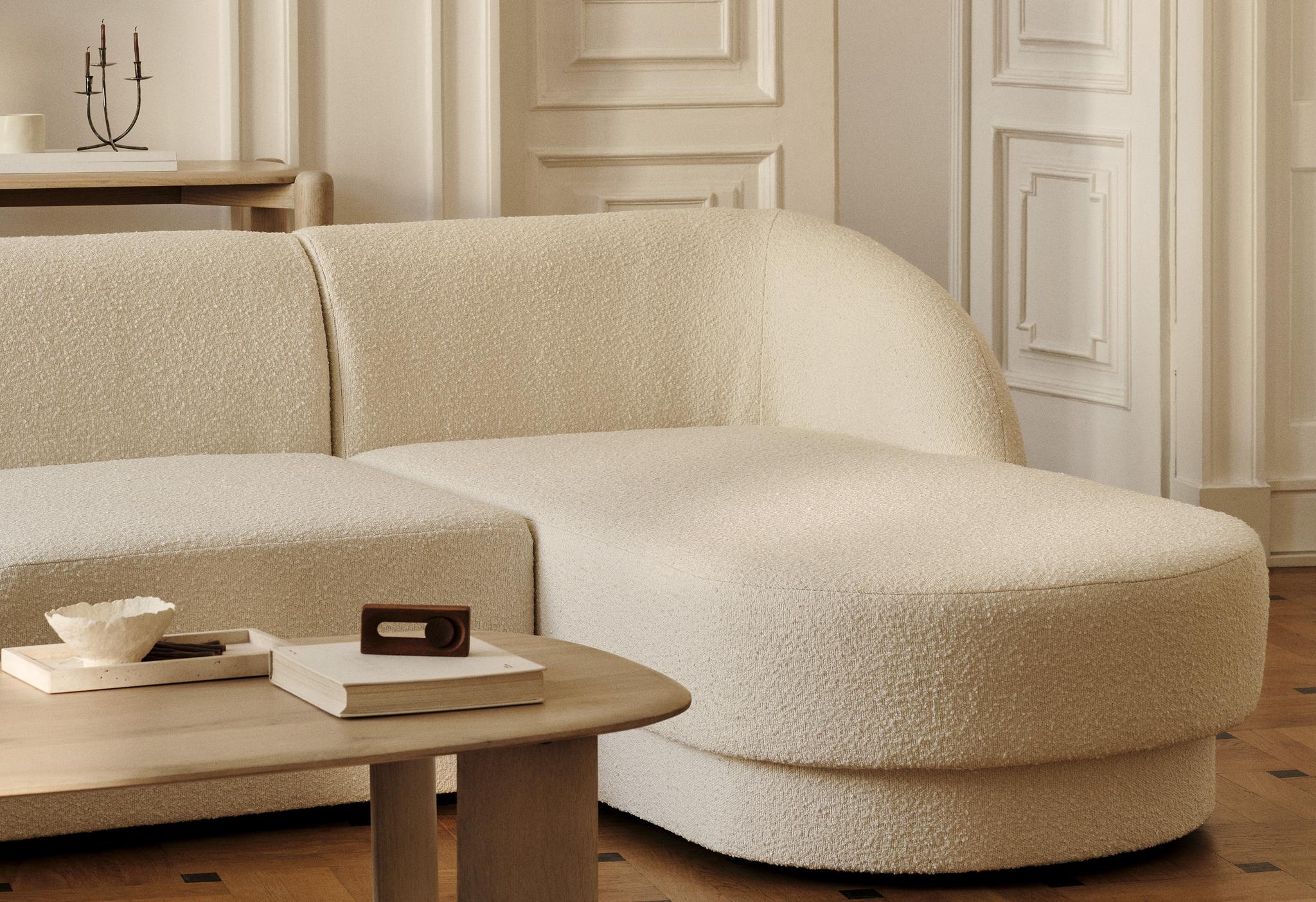 Canapé d’angle Miley en tissu bouclé crème aux bords arrondis, associé à une table basse ovale Aggie en bois – mobilier Micadoni
