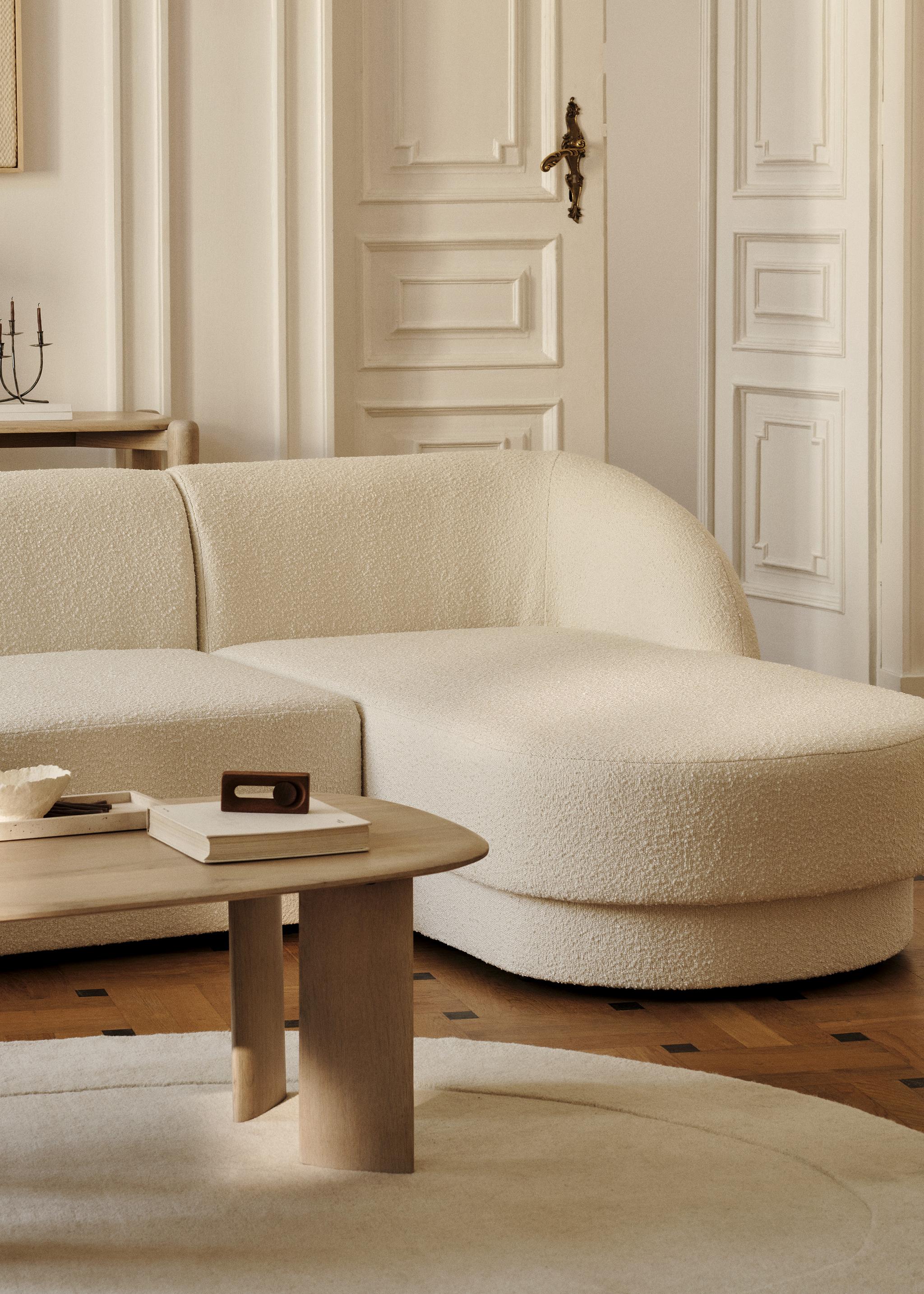 Canapé d’angle Miley en tissu bouclé crème aux bords arrondis, associé à une table basse ovale Aggie en bois – mobilier Micadoni