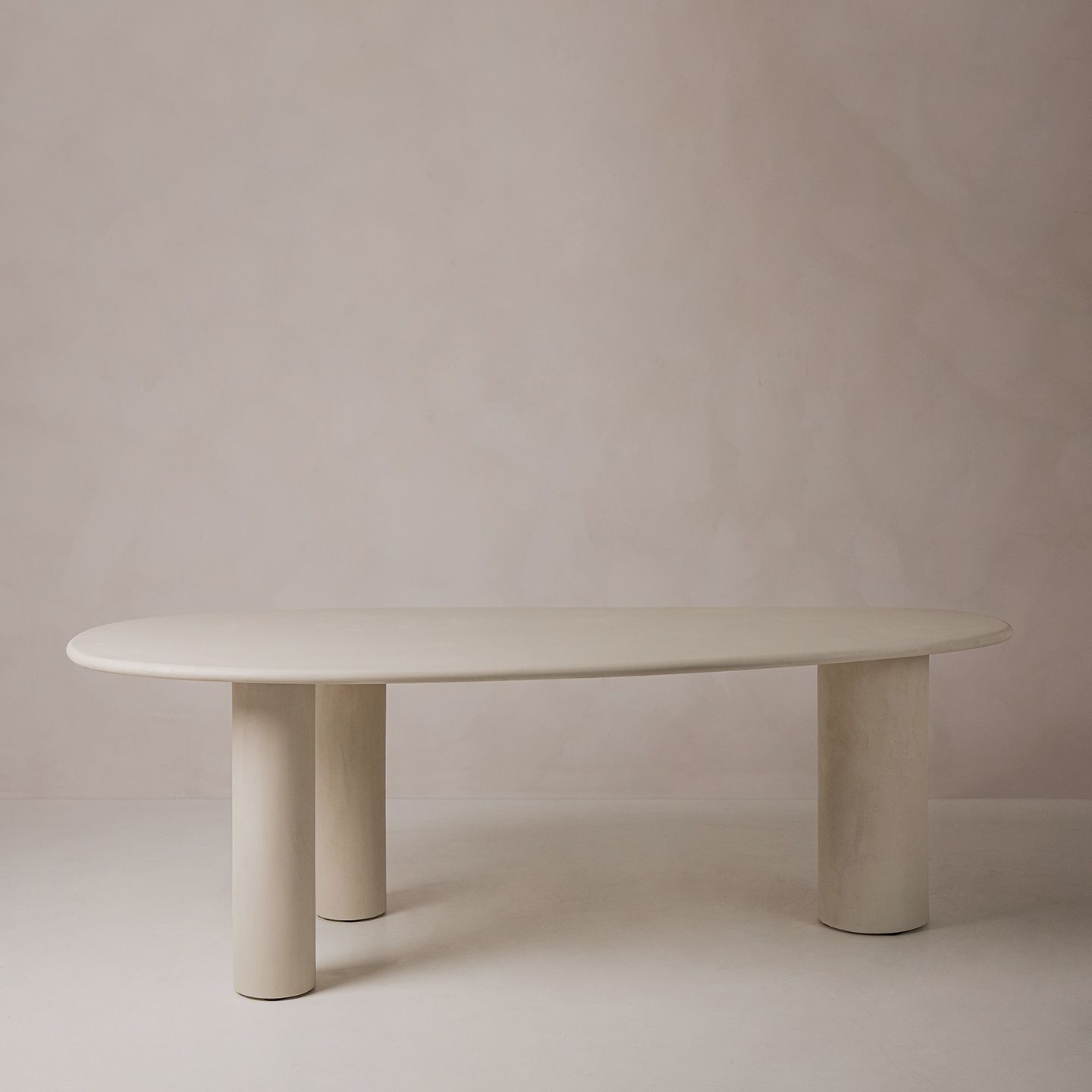 Table de salle à manger Micadoni, plateau ovale et trois pieds cylindriques, finition beige mate, fond studio.