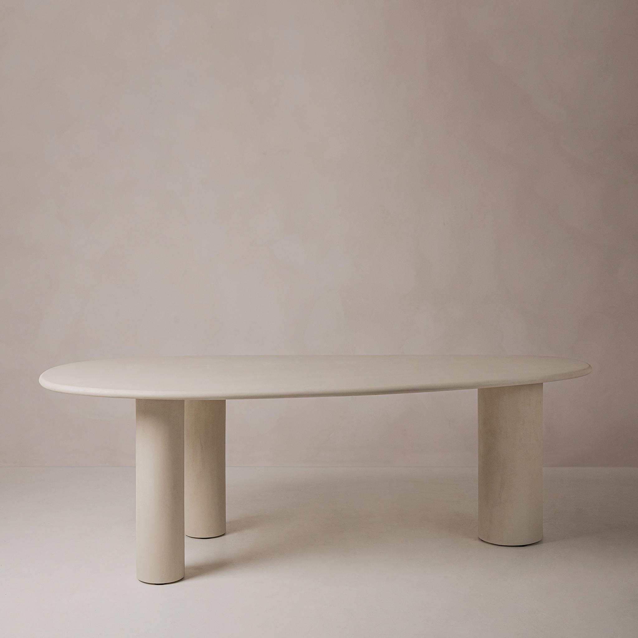 Table de salle à manger Micadoni, plateau ovale et trois pieds cylindriques, finition beige mate, fond studio.