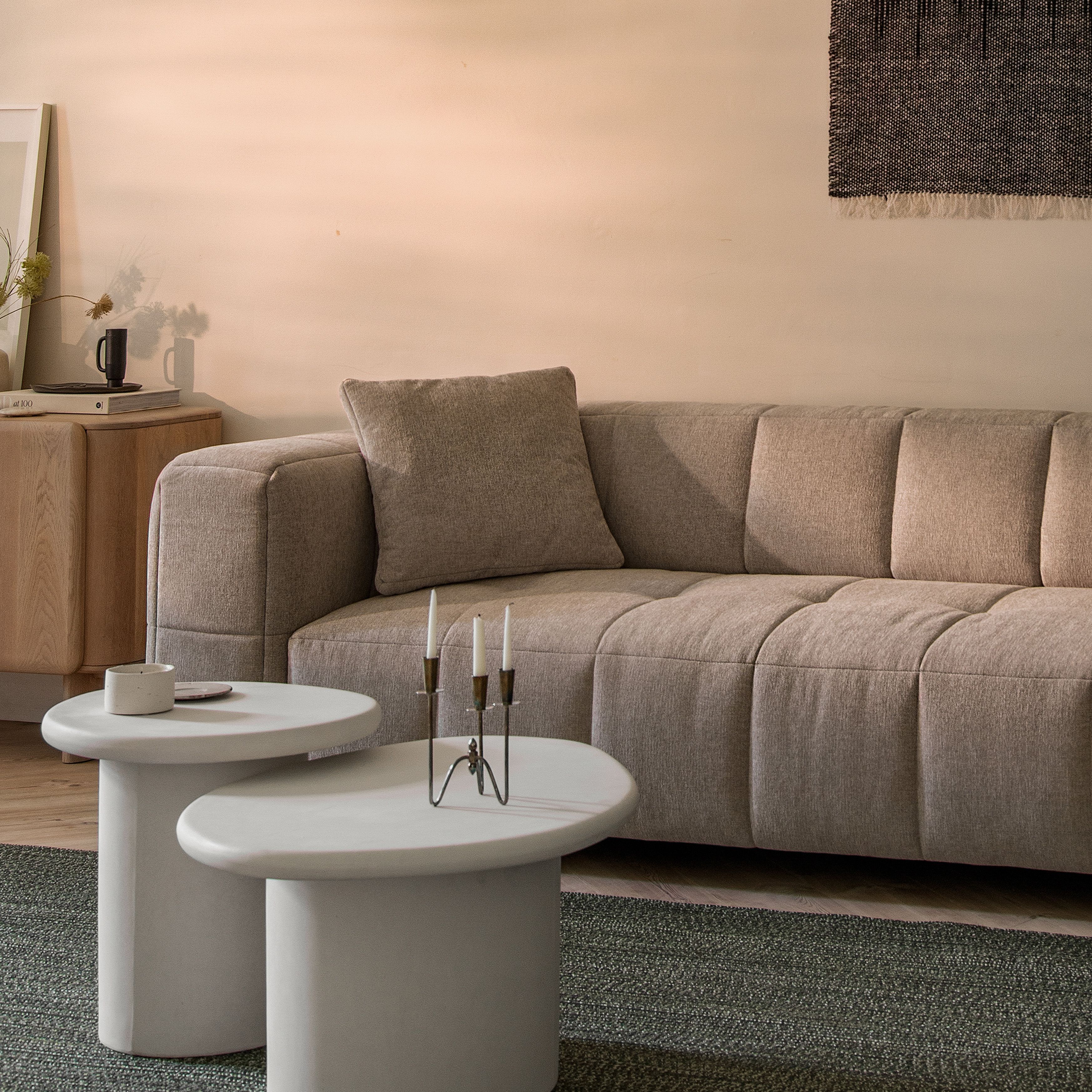 Canapé Bemy de Micadoni en tissu texturé taupe clair, capitonnage carré doux et accoudoirs bas, présenté avec deux tables basses blanches sur un tapis vert.