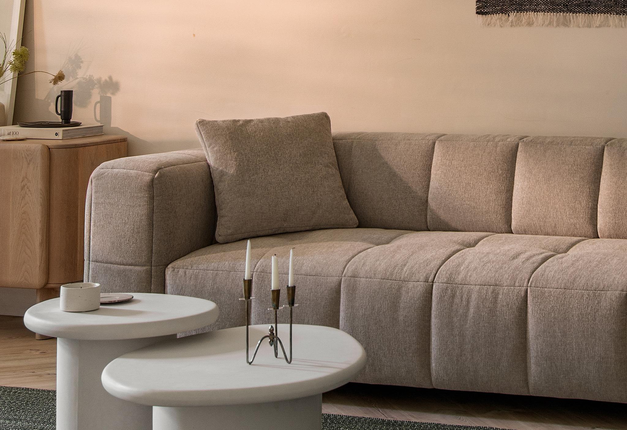 Canapé Bemy de Micadoni en tissu texturé taupe clair, capitonnage carré doux et accoudoirs bas, présenté avec deux tables basses blanches sur un tapis vert.