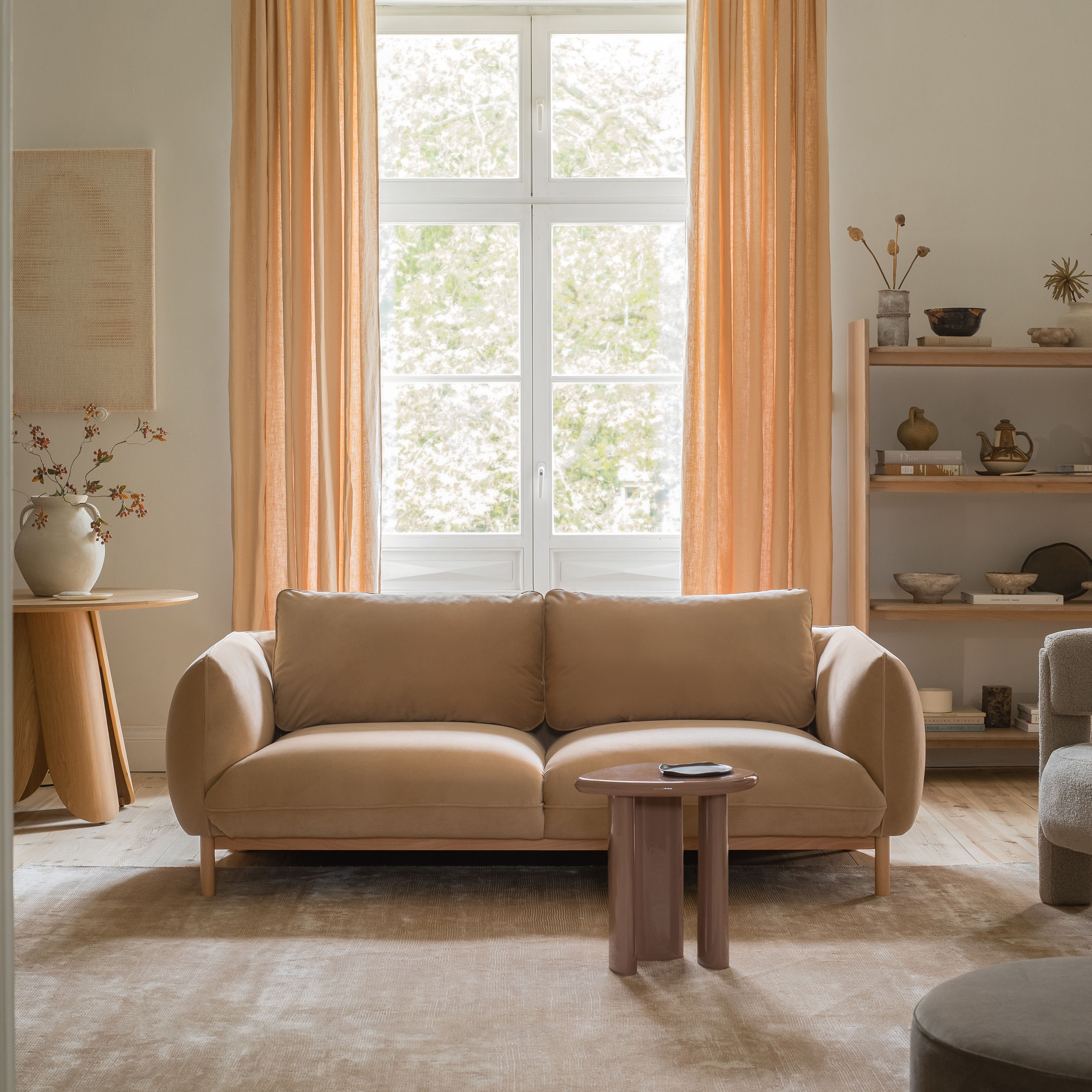 : Canapé deux places Micadoni Ada en tissu beige, accoudoirs arrondis, dans un salon lumineux.