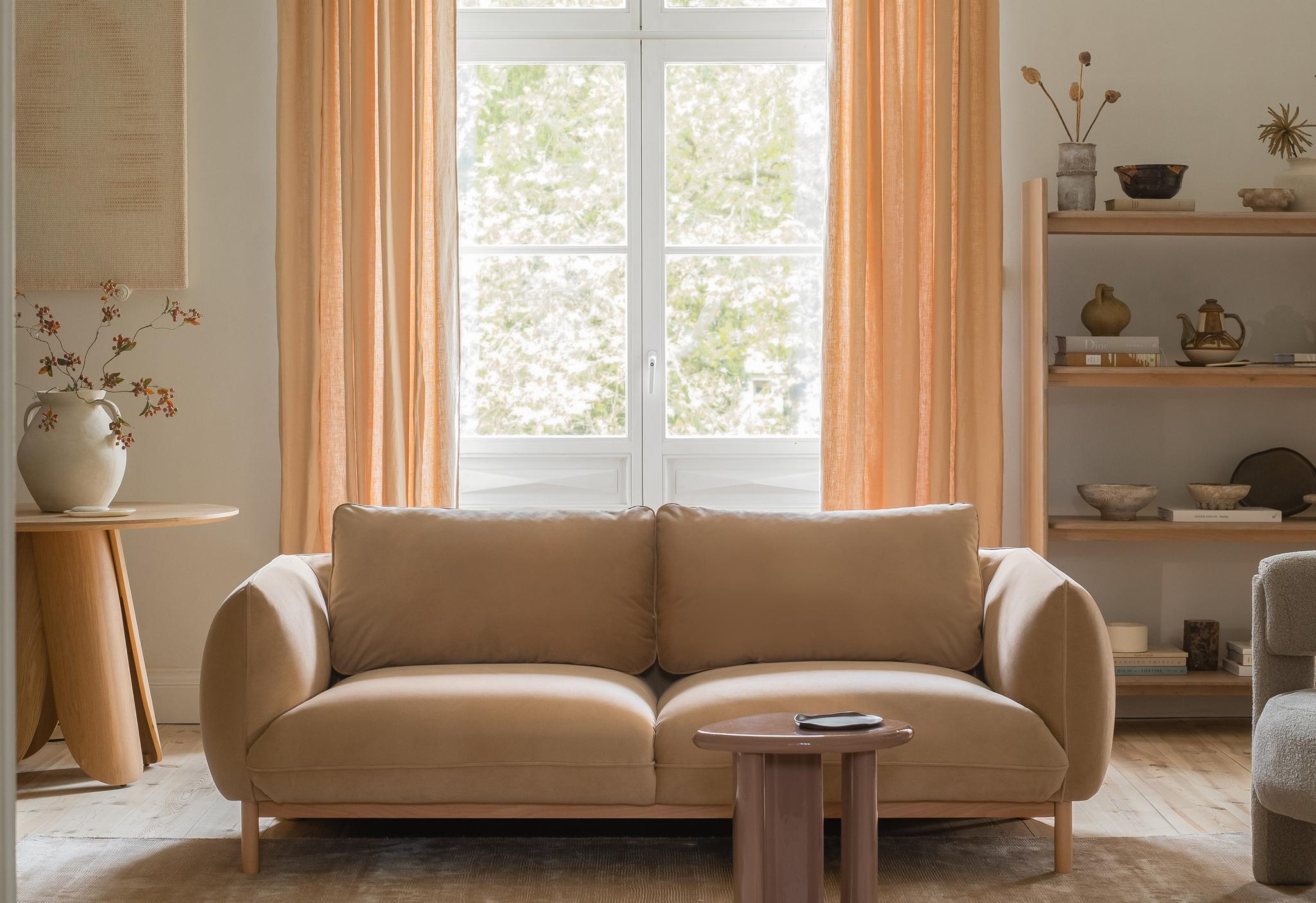 : Canapé deux places Micadoni Ada en tissu beige, accoudoirs arrondis, dans un salon lumineux.