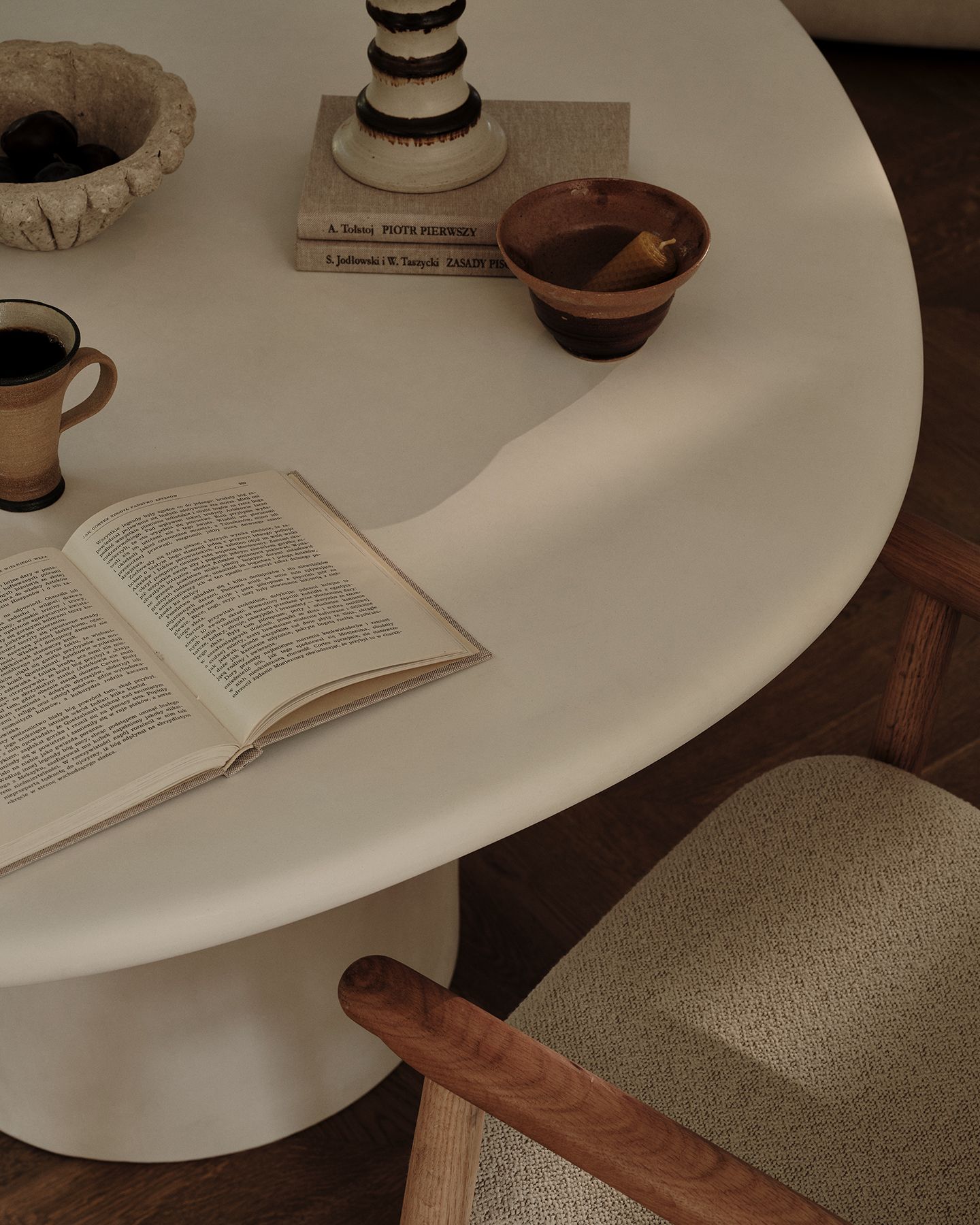 Table de salle à manger Micadoni Daria dans une ambiance chaleureuse, avec céramiques, livre ouvert et fauteuil texturé.
