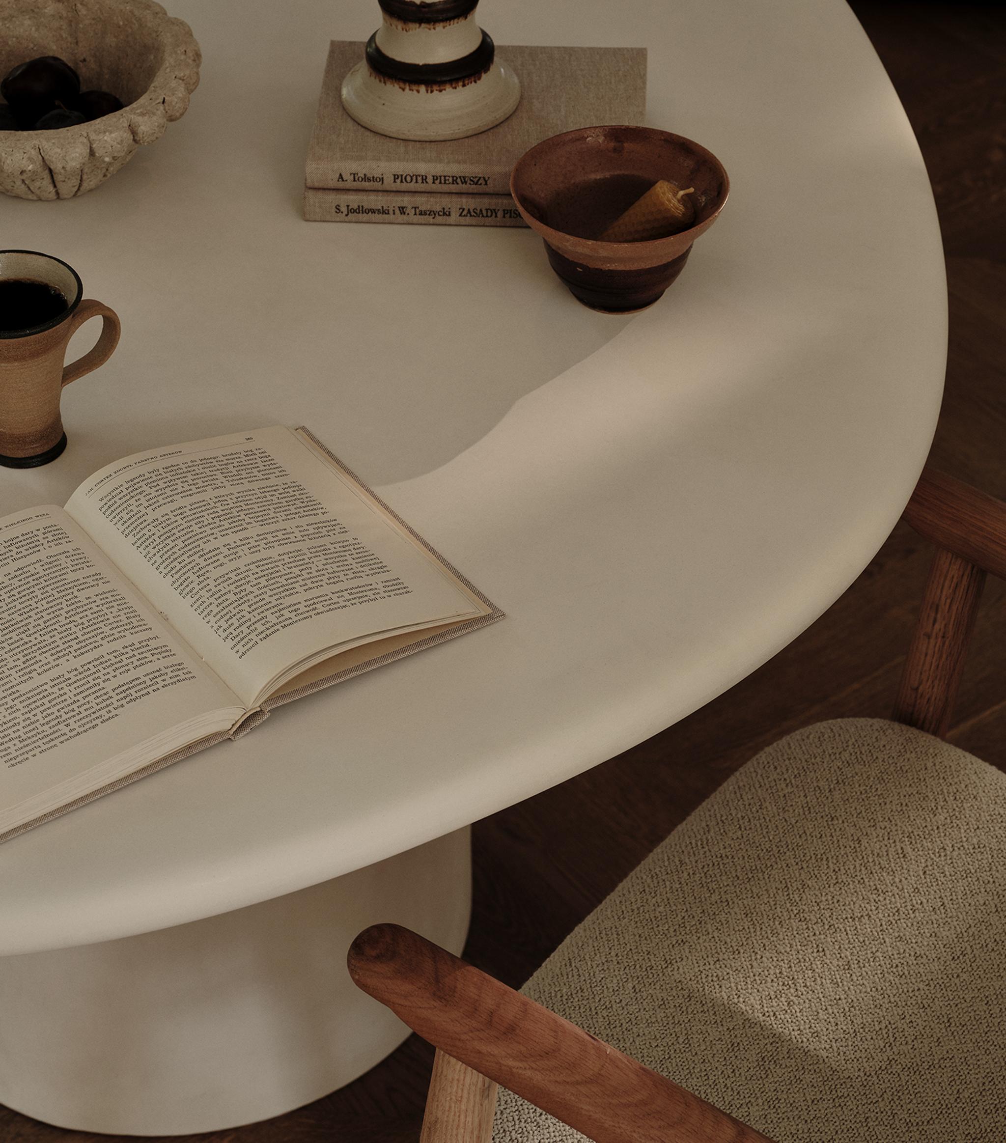 Table de salle à manger Micadoni Daria dans une ambiance chaleureuse, avec céramiques, livre ouvert et fauteuil texturé.