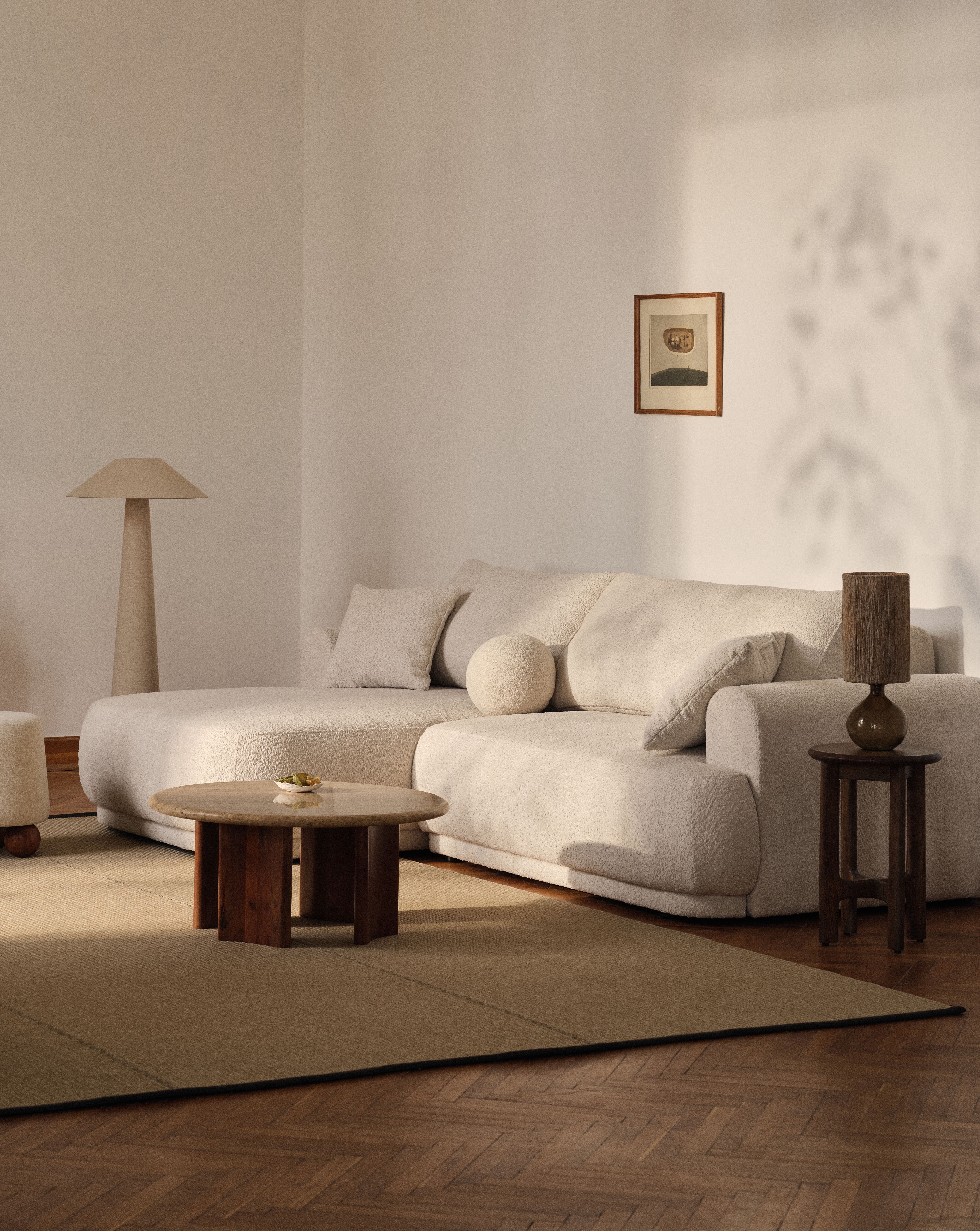 Canapé Micadoni Ella en bouclé écru avec méridienne, coussin rond, table basse et lampes.