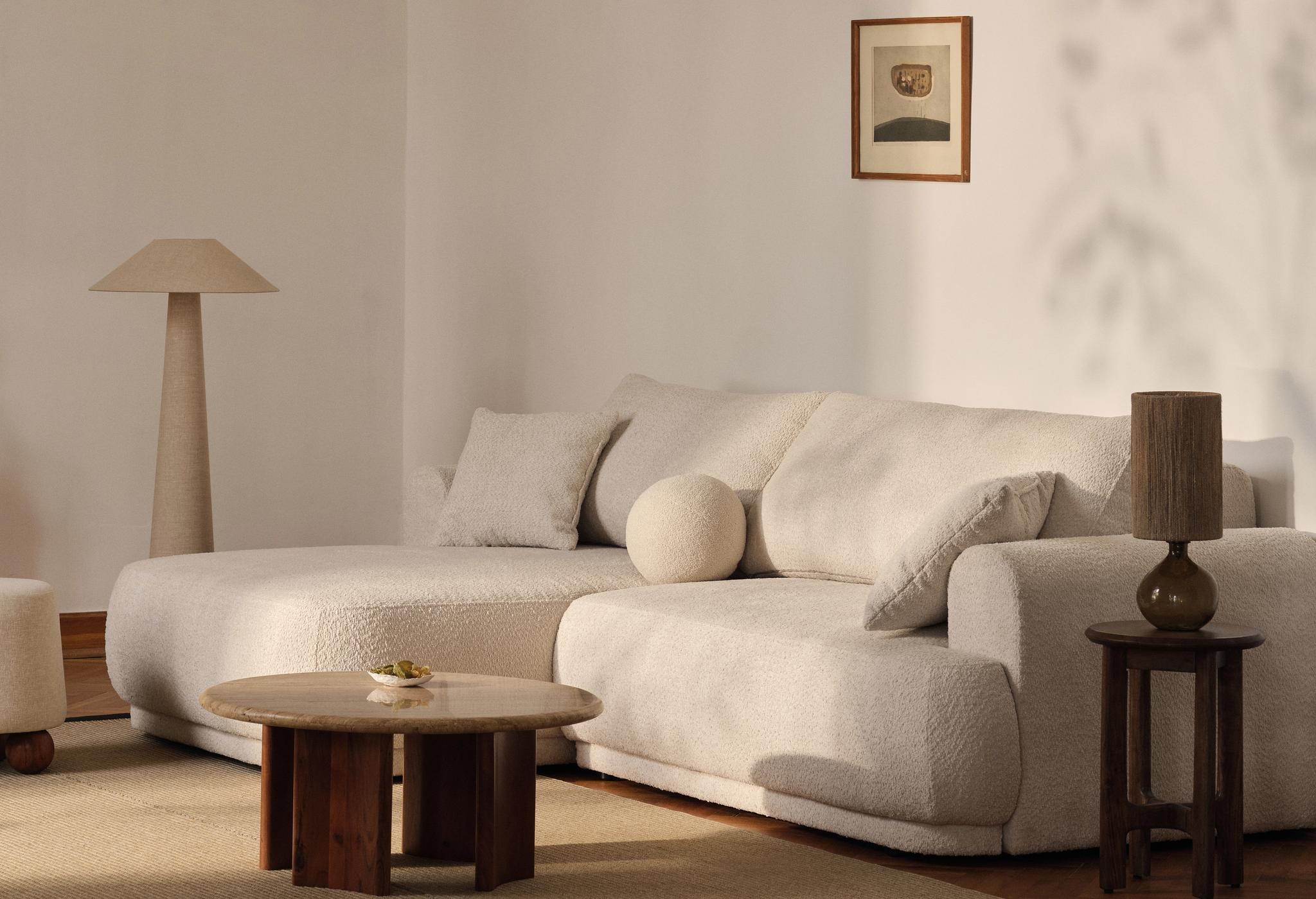 Canapé Micadoni Ella en bouclé écru avec méridienne, coussin rond, table basse et lampes.