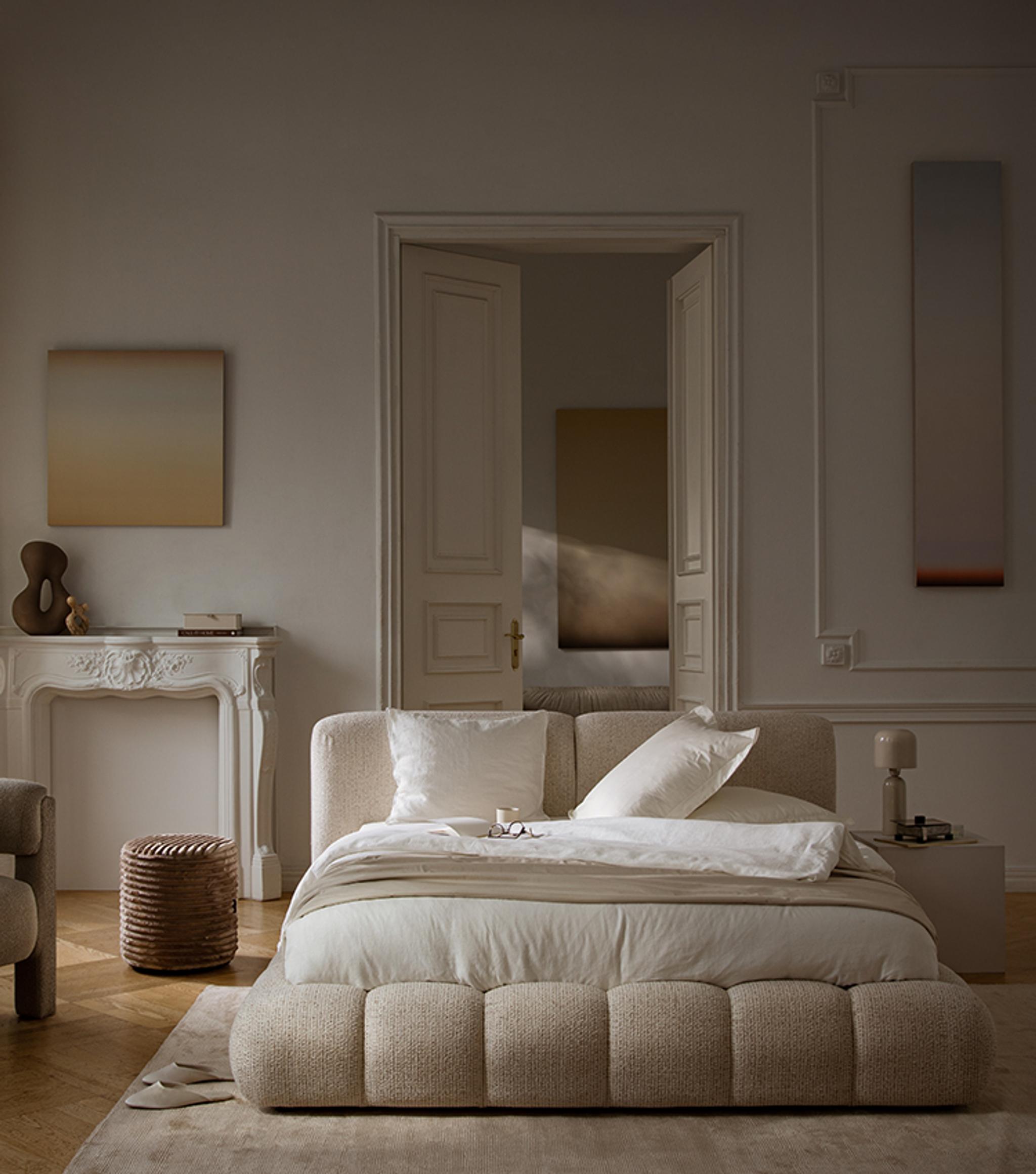 Lit Micadoni Lupine en revêtement rouille chaleureux avec tête de lit à coutures verticales, mis en scène dans une chambre aux tons doux avec tapis rond crème, table d’appoint et lampe de table.