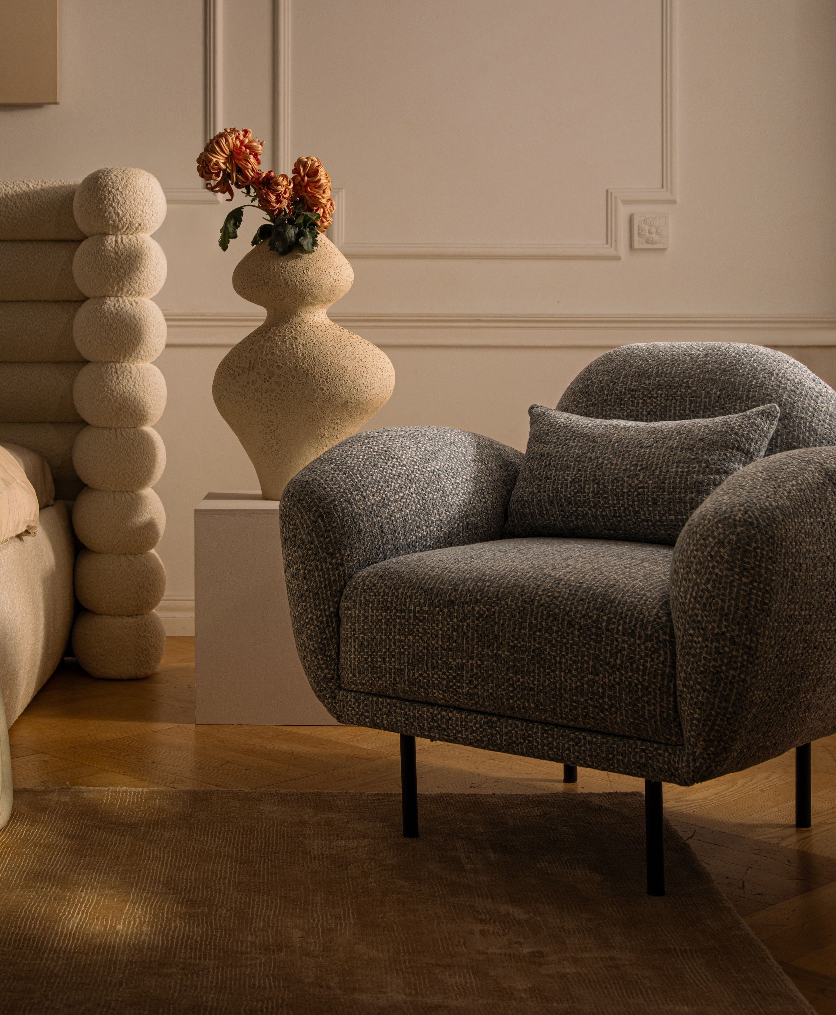 Canapé Poppy de Micadoni en bouclé brun foncé, accoudoirs arrondis et pieds noirs fins, présenté dans un salon minimaliste et chaleureux.