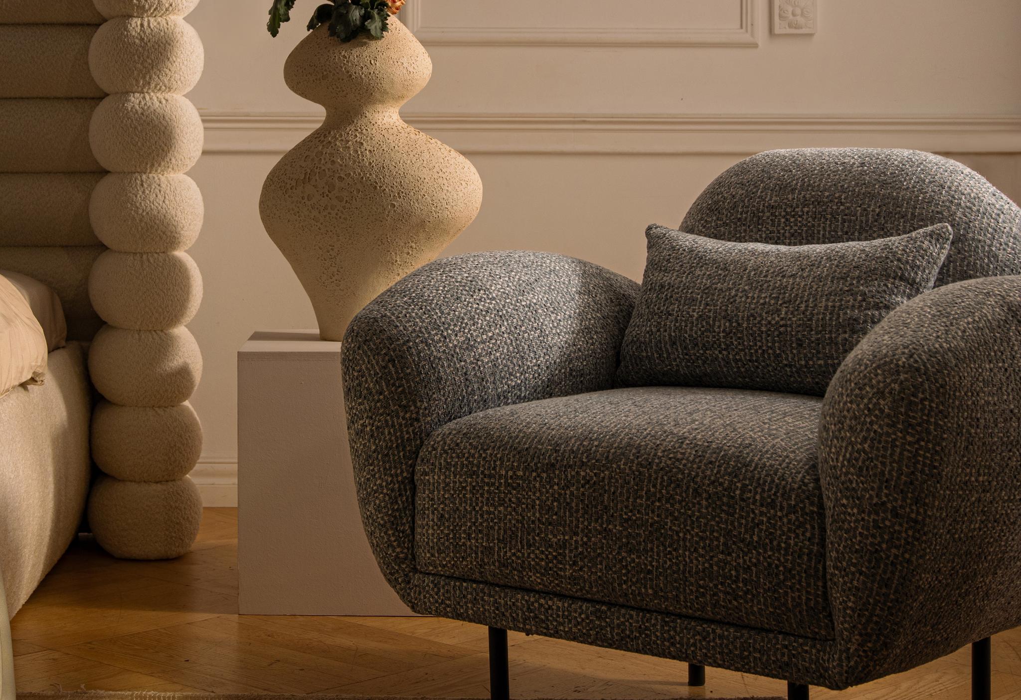 Canapé Poppy de Micadoni en bouclé brun foncé, accoudoirs arrondis et pieds noirs fins, présenté dans un salon minimaliste et chaleureux.