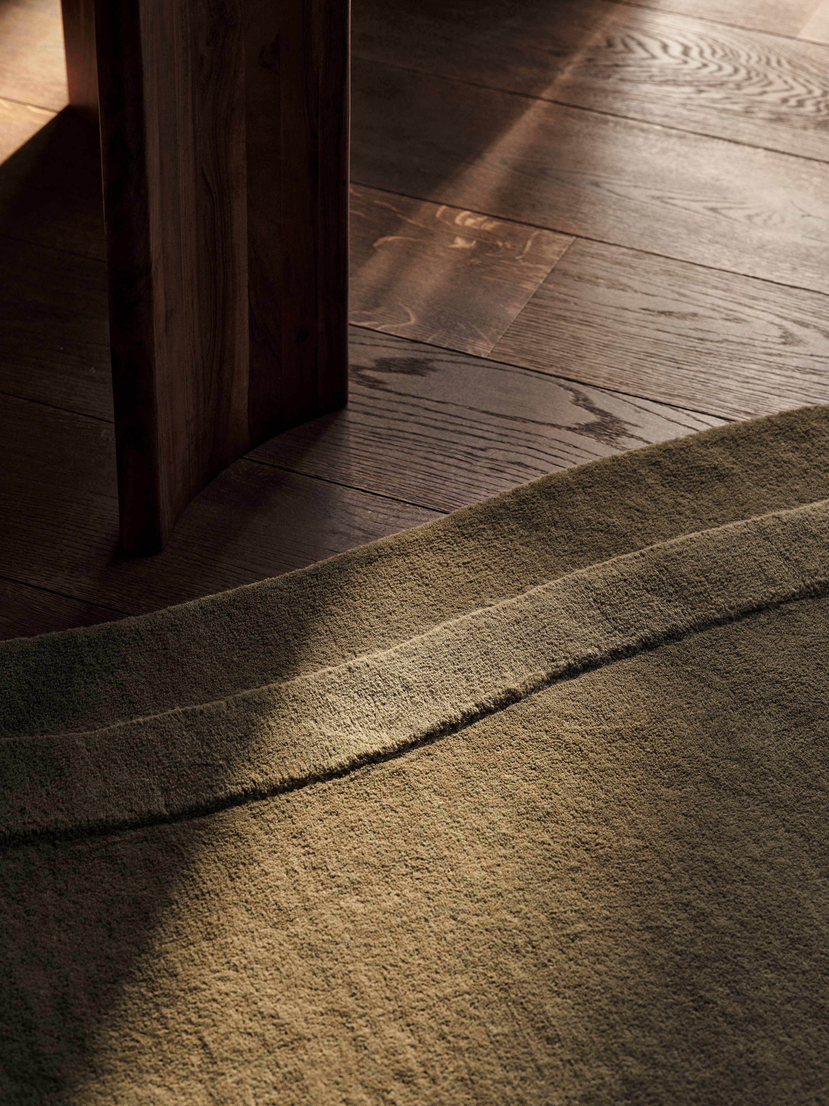 Tapis Micadoni vert olive texturé, gros plan sur le bord sculpté sur parquet.