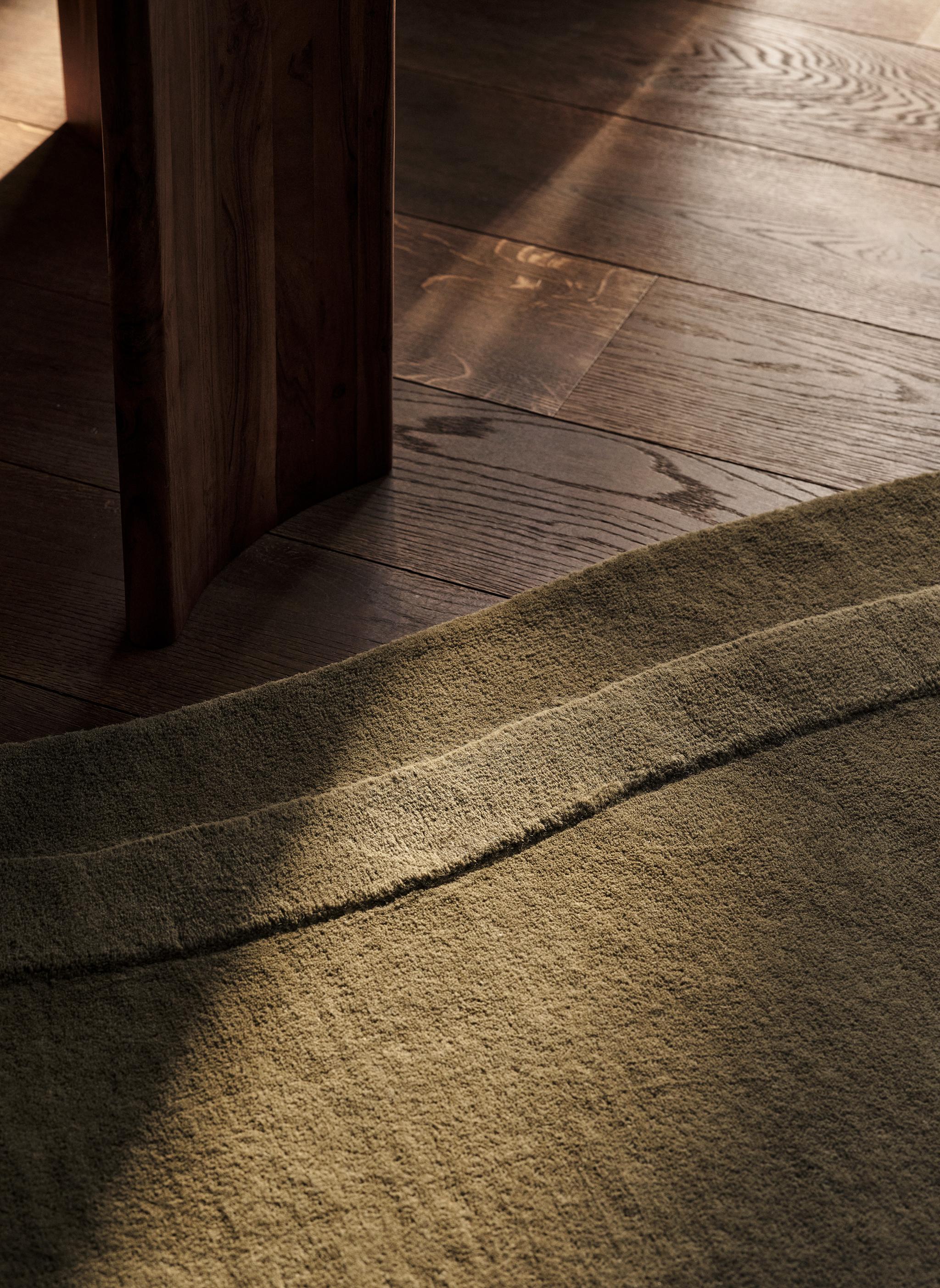 Tapis Micadoni vert olive texturé, gros plan sur le bord sculpté sur parquet.