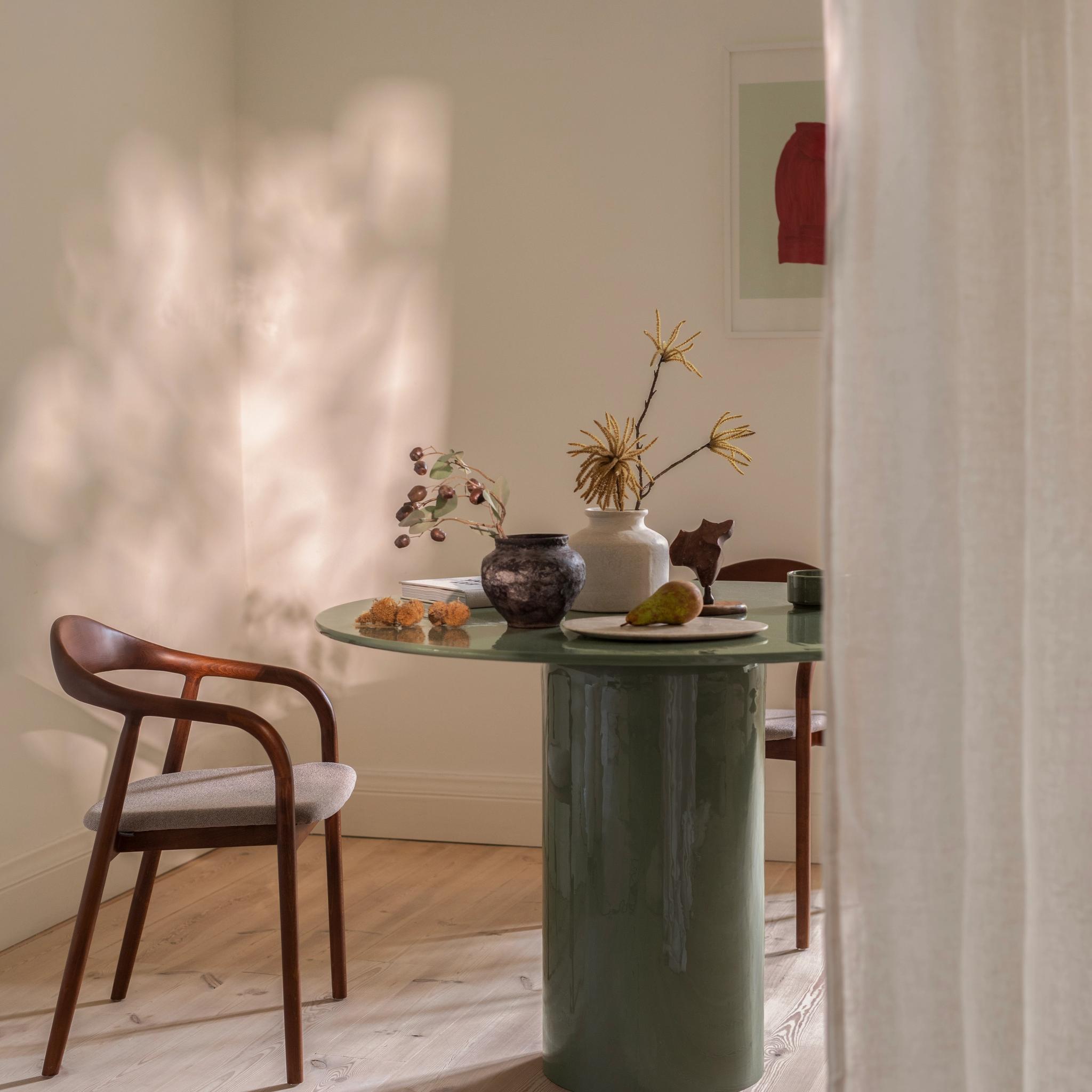 able de repas Micadoni ronde vert olive, piètement colonne laqué, avec chaise Illa en bois courbé et assise beige, pièce baignée de soleil.