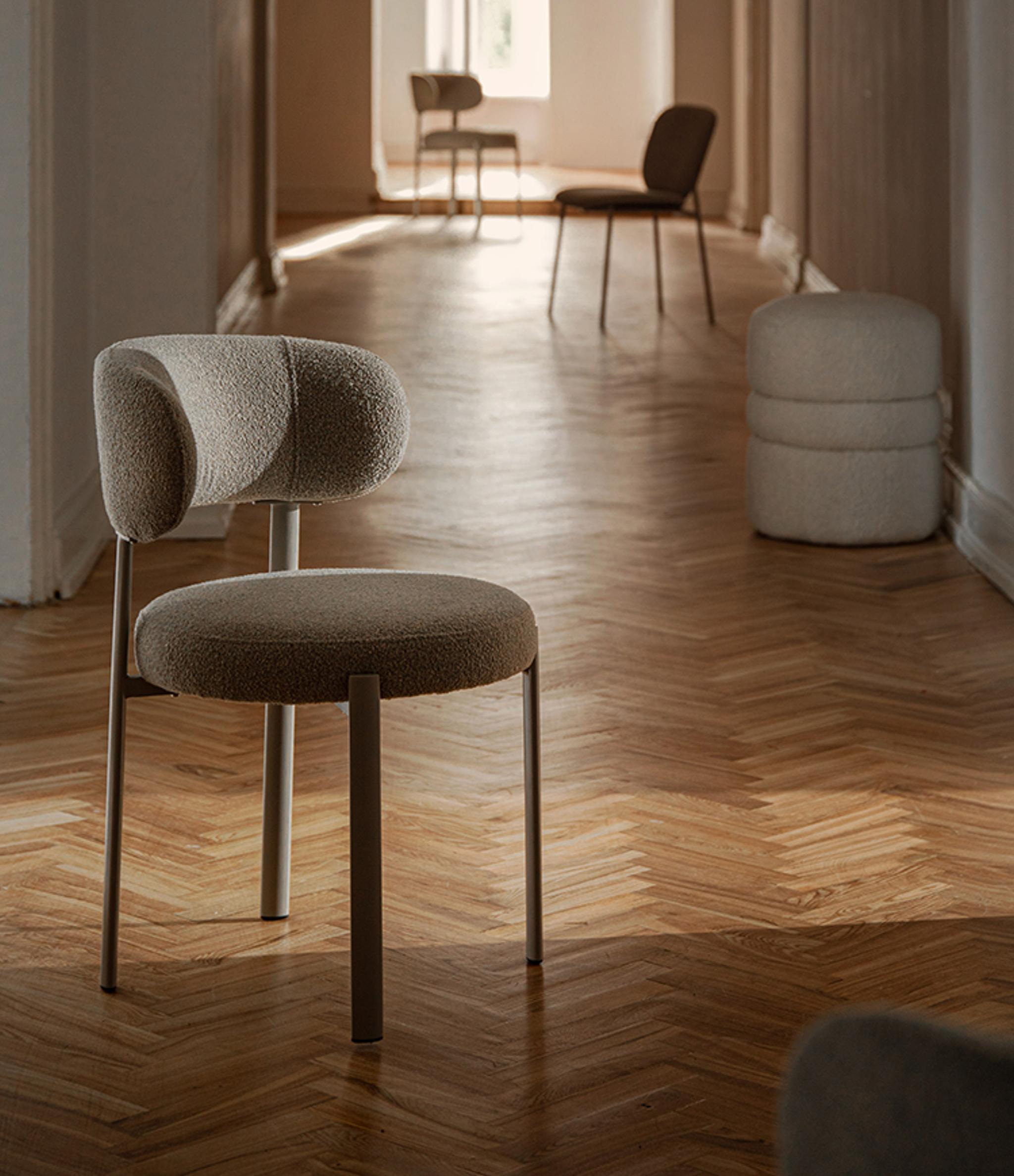 Chaise Micadoni tapissée en bouclé, dossier arrondi et pieds métal, dans un couloir lumineux au parquet en chevrons.