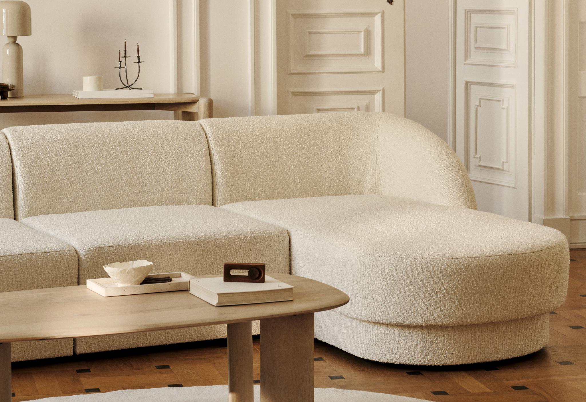 Canapé d’angle Miley en tissu bouclé crème aux bords arrondis, associé à une table basse ovale Aggie en bois – mobilier Micadoni