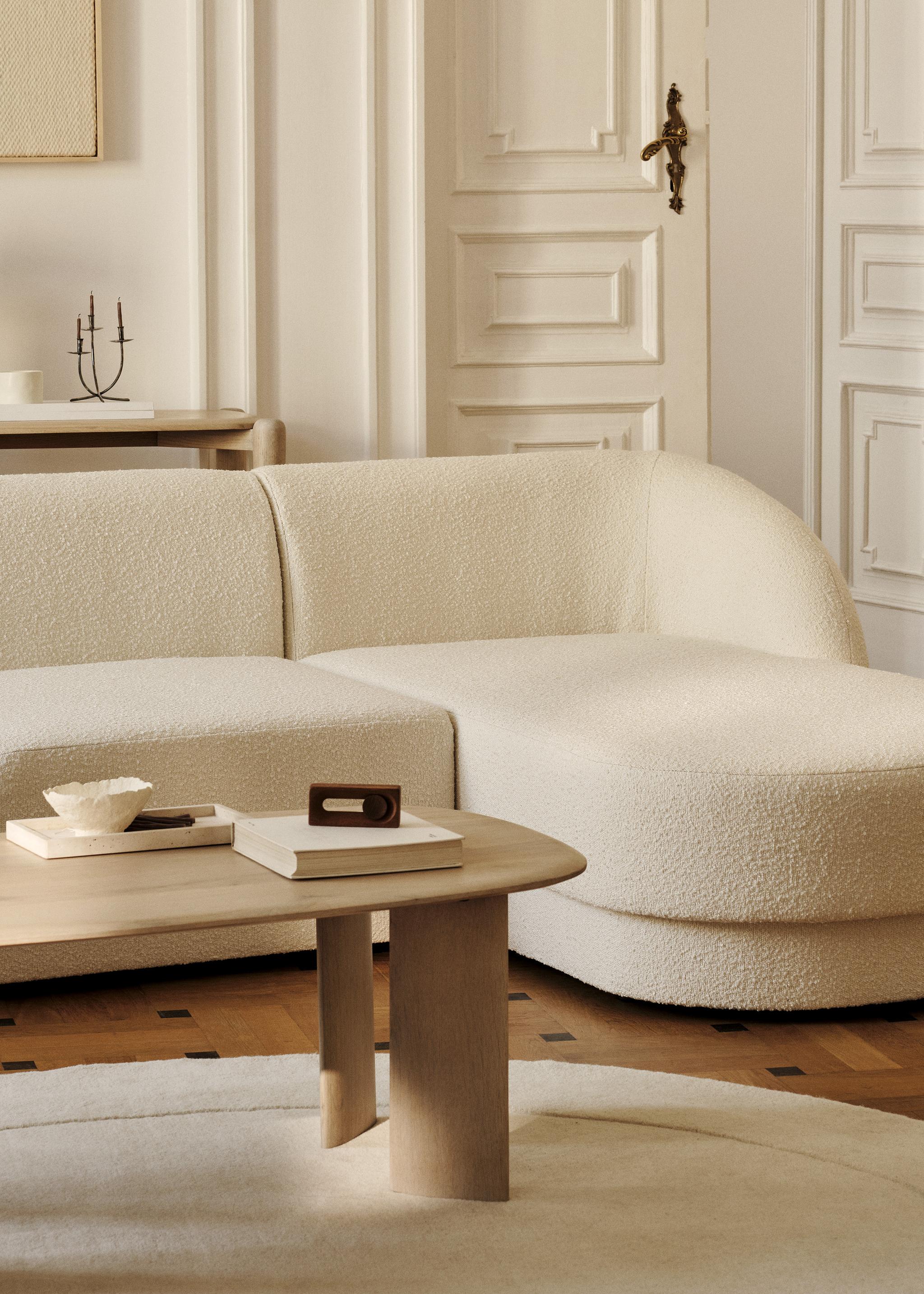 Canapé d’angle Miley en tissu bouclé crème aux bords arrondis, associé à une table basse ovale Aggie en bois – mobilier Micadoni