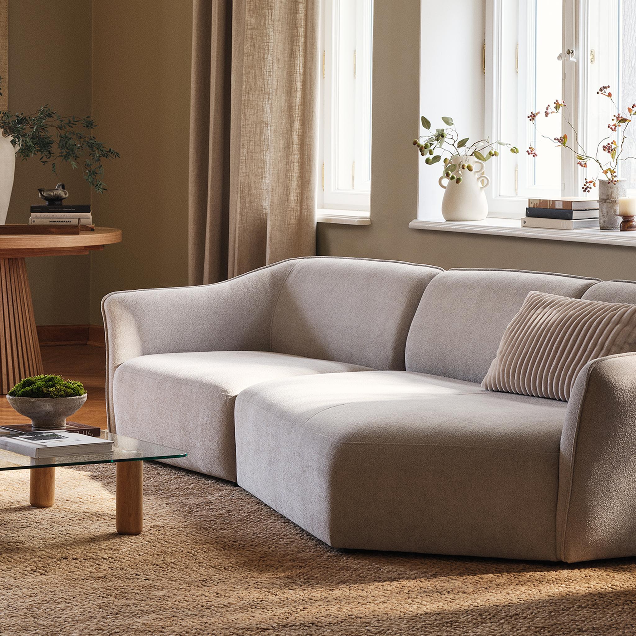 Canapé Hailey de Micadoni avec table basse Moscarte en verre et table à manger ronde Portmany en bois dans un salon chaleureux et ensoleillé