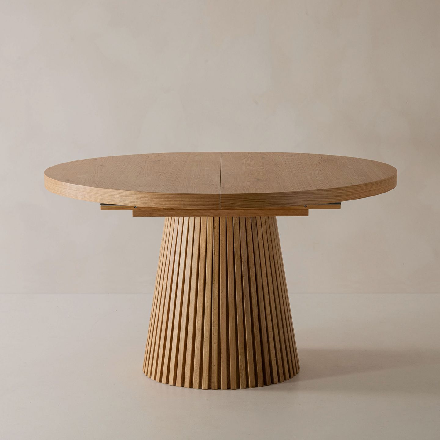 Gros plan d’une table de salle à manger Micadoni ronde et extensible en chêne, avec piètement cannelé et joint central visible.