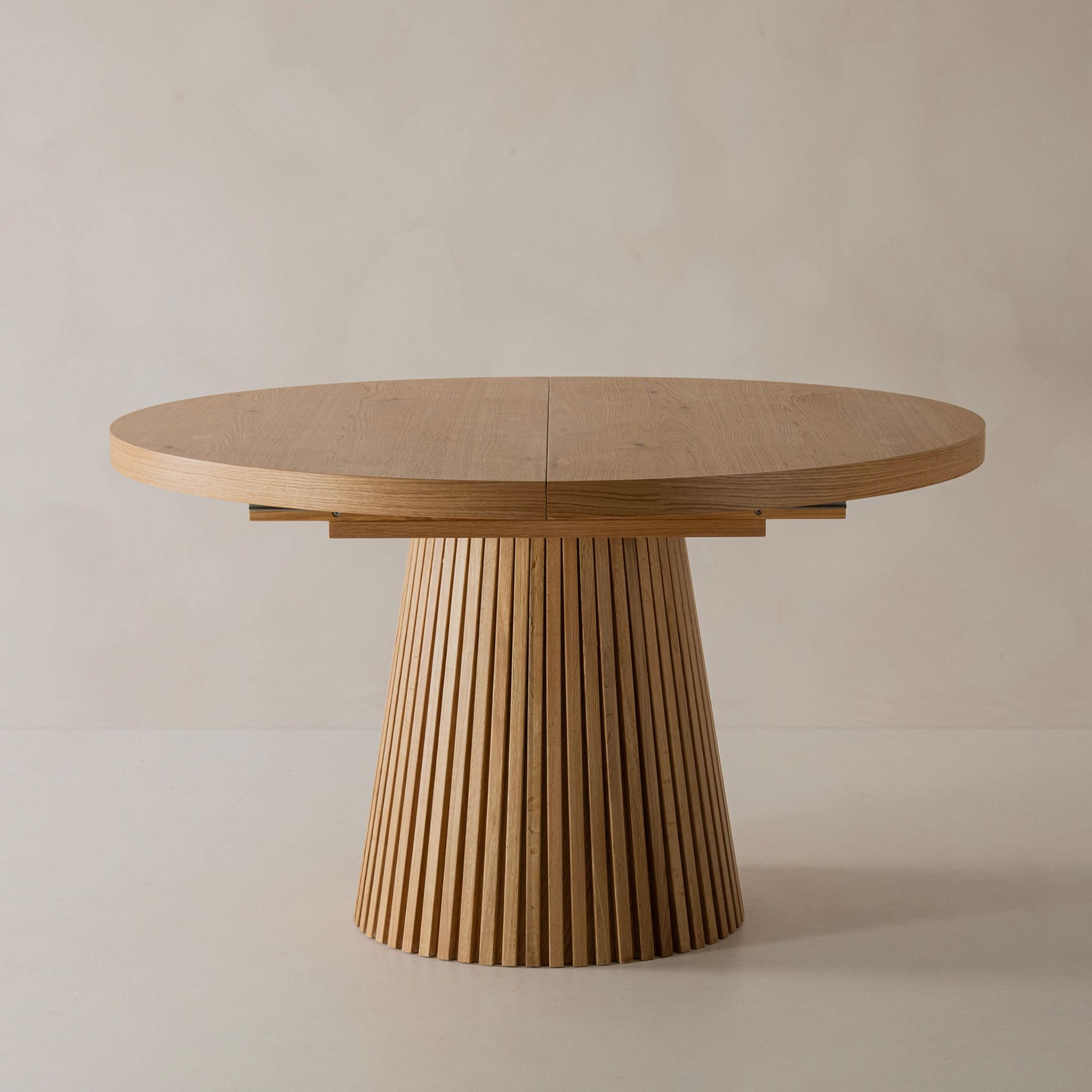 Gros plan d’une table de salle à manger Micadoni ronde et extensible en chêne, avec piètement cannelé et joint central visible.