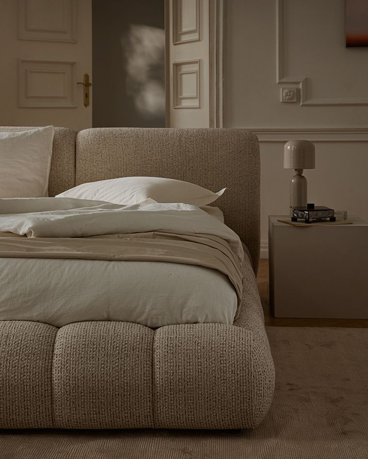 Lit Micadoni Martina avec base capitonnée arrondie et grande tête de lit texturée dans une chambre chaleureuse.