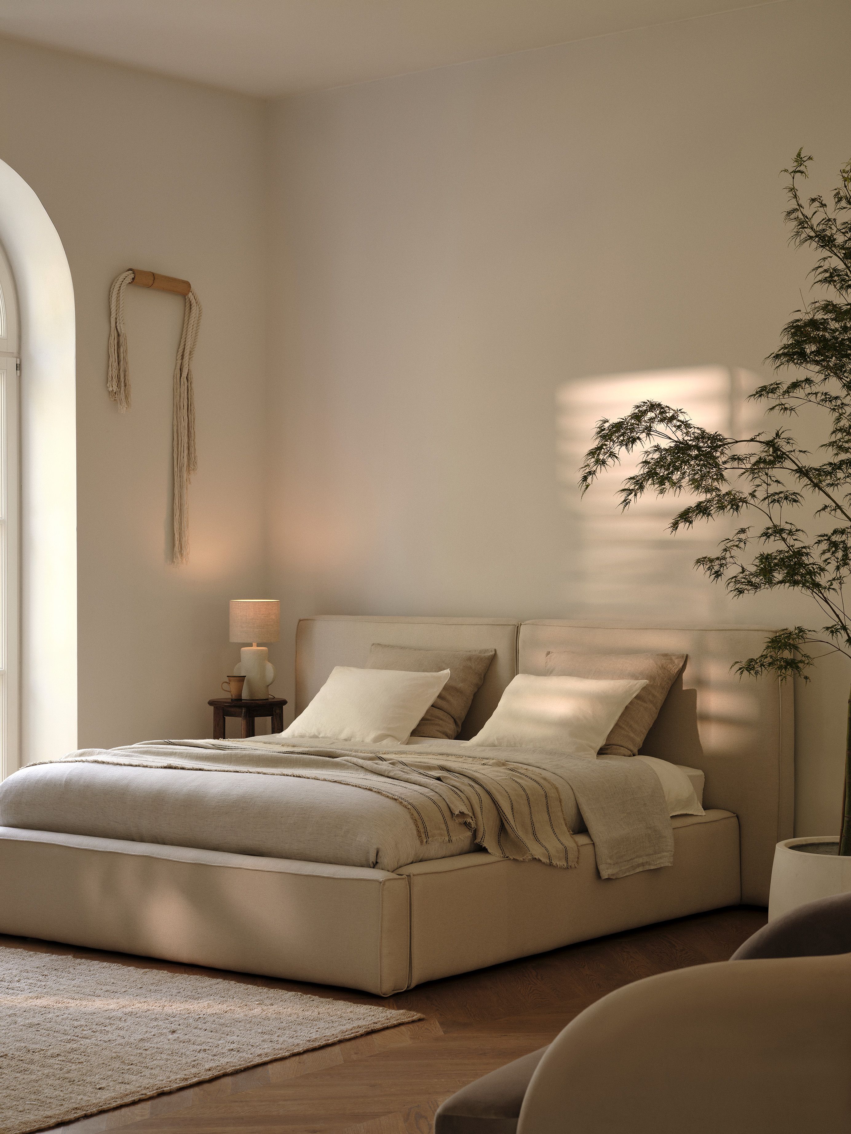 Lit Micadoni capitonné en tissu beige avec tête de lit rembourrée dans une chambre apaisante.