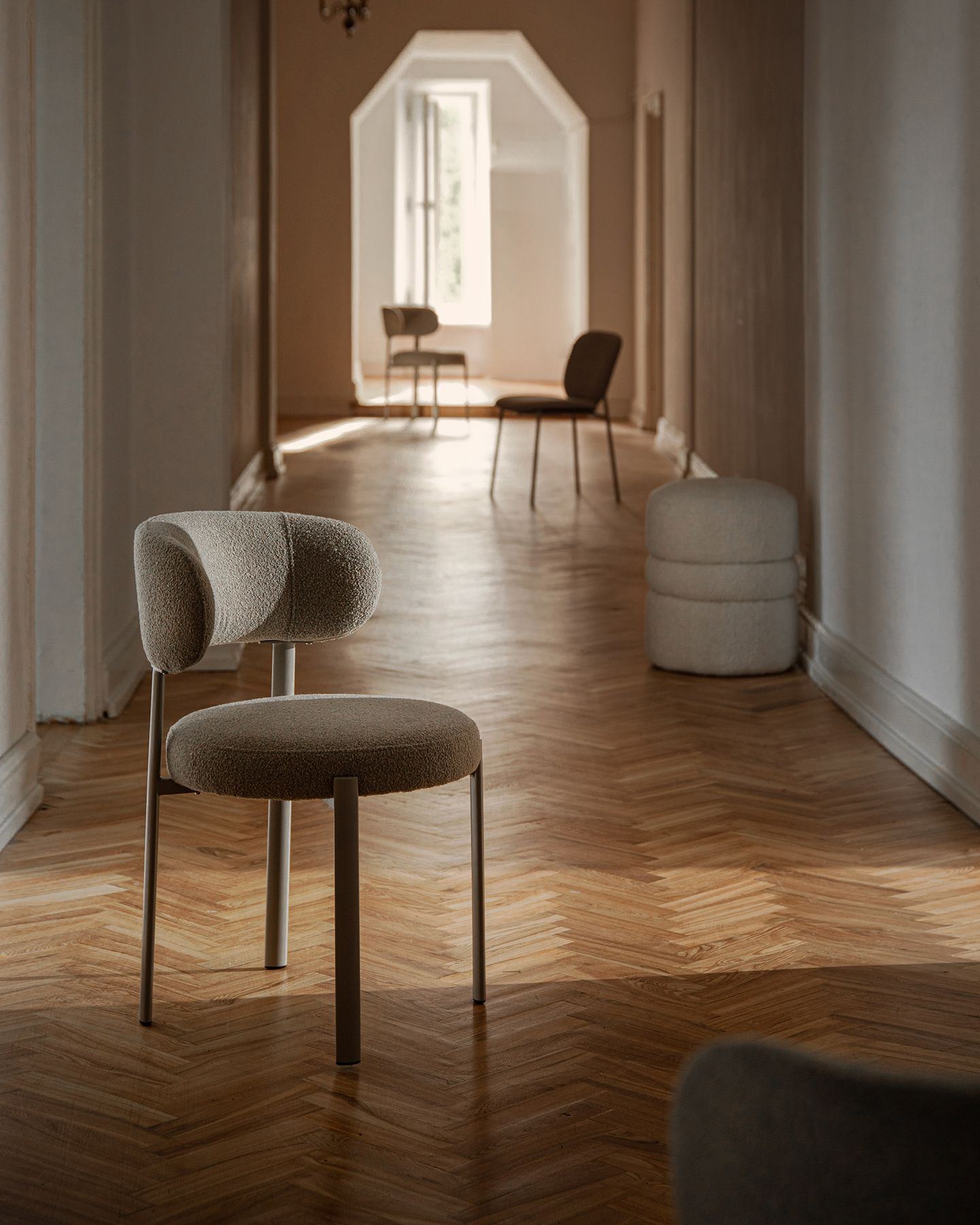 Chaise Micadoni tapissée en bouclé, dossier arrondi et pieds métal, dans un couloir lumineux au parquet en chevrons.
