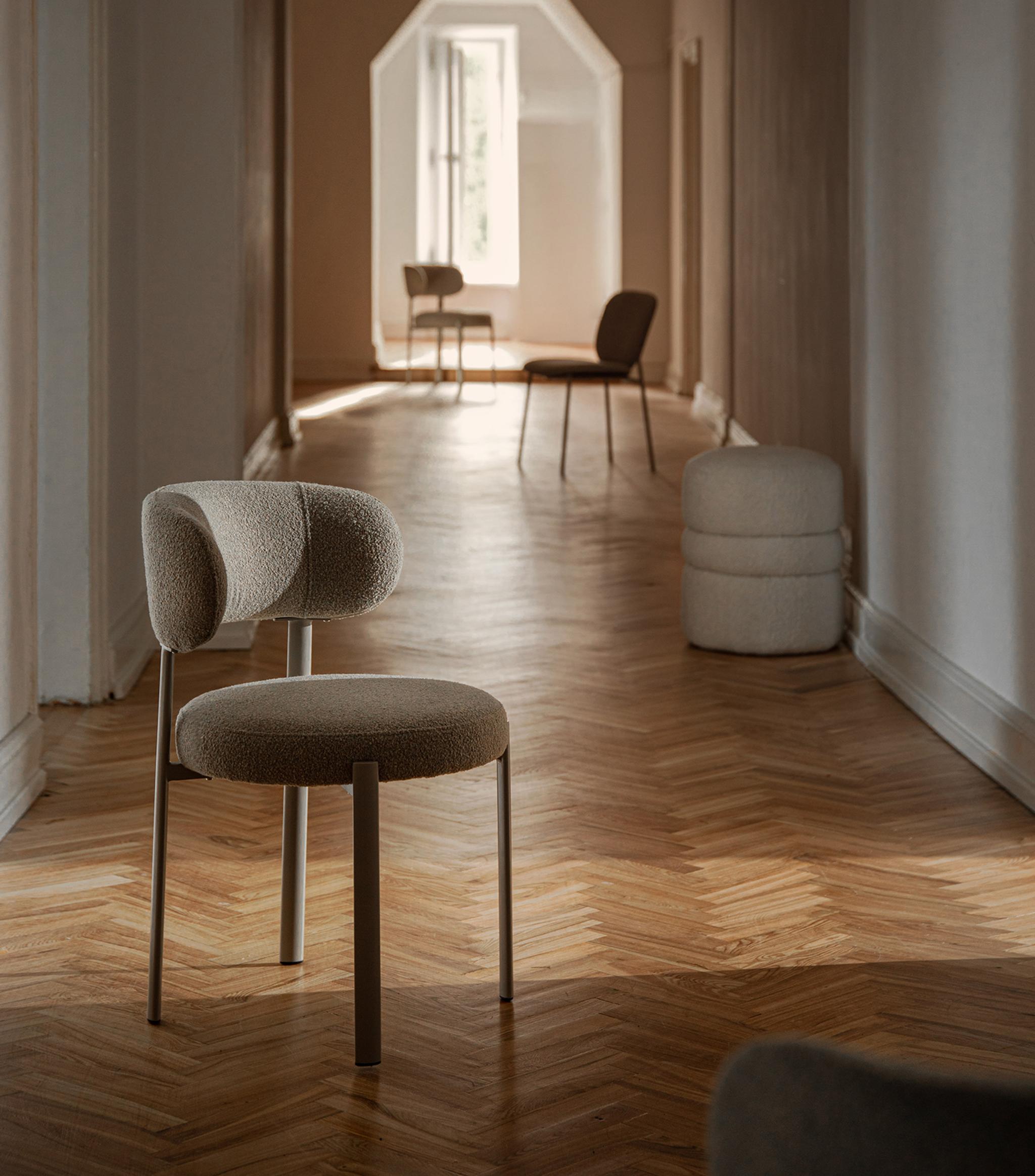 Chaise Micadoni tapissée en bouclé, dossier arrondi et pieds métal, dans un couloir lumineux au parquet en chevrons.