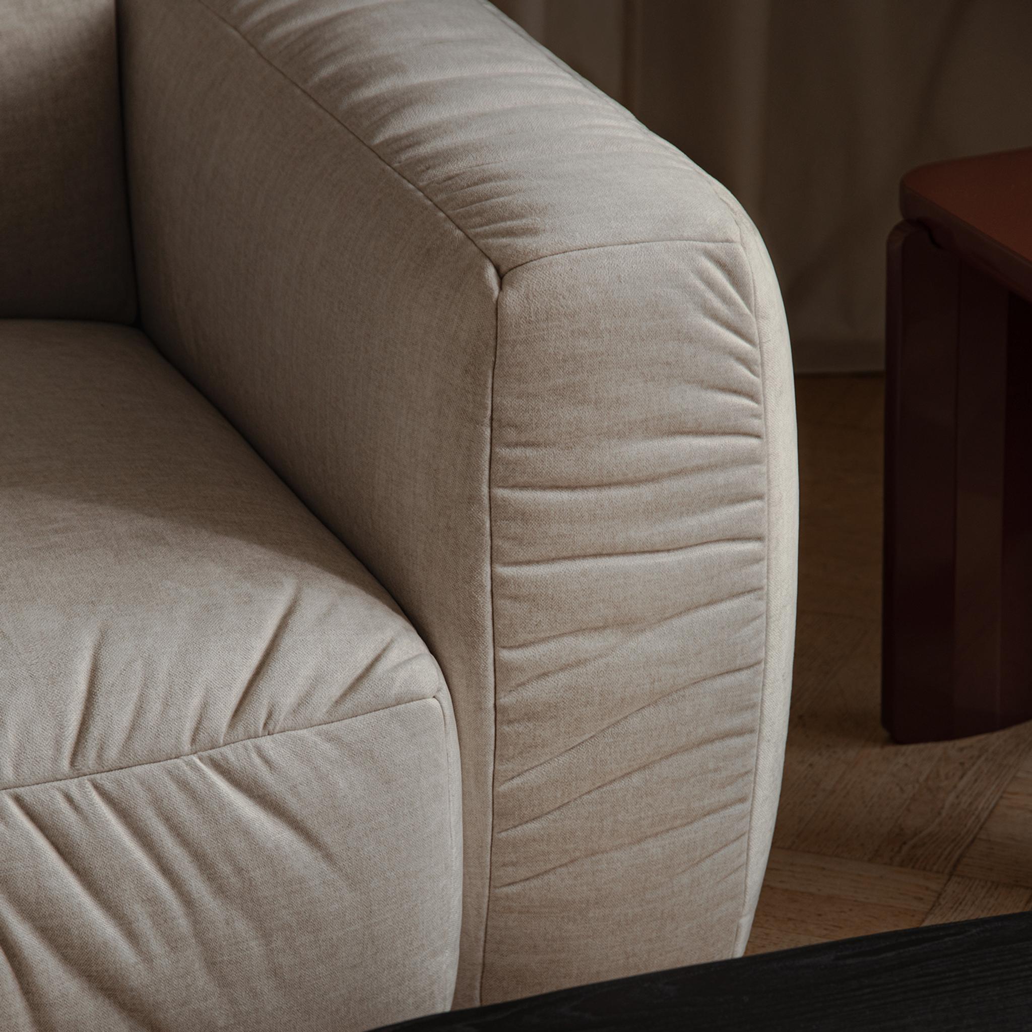 Gros plan sur un canapé Micadoni : accoudoir et dossier arrondis en tissu beige clair à tissage serré.