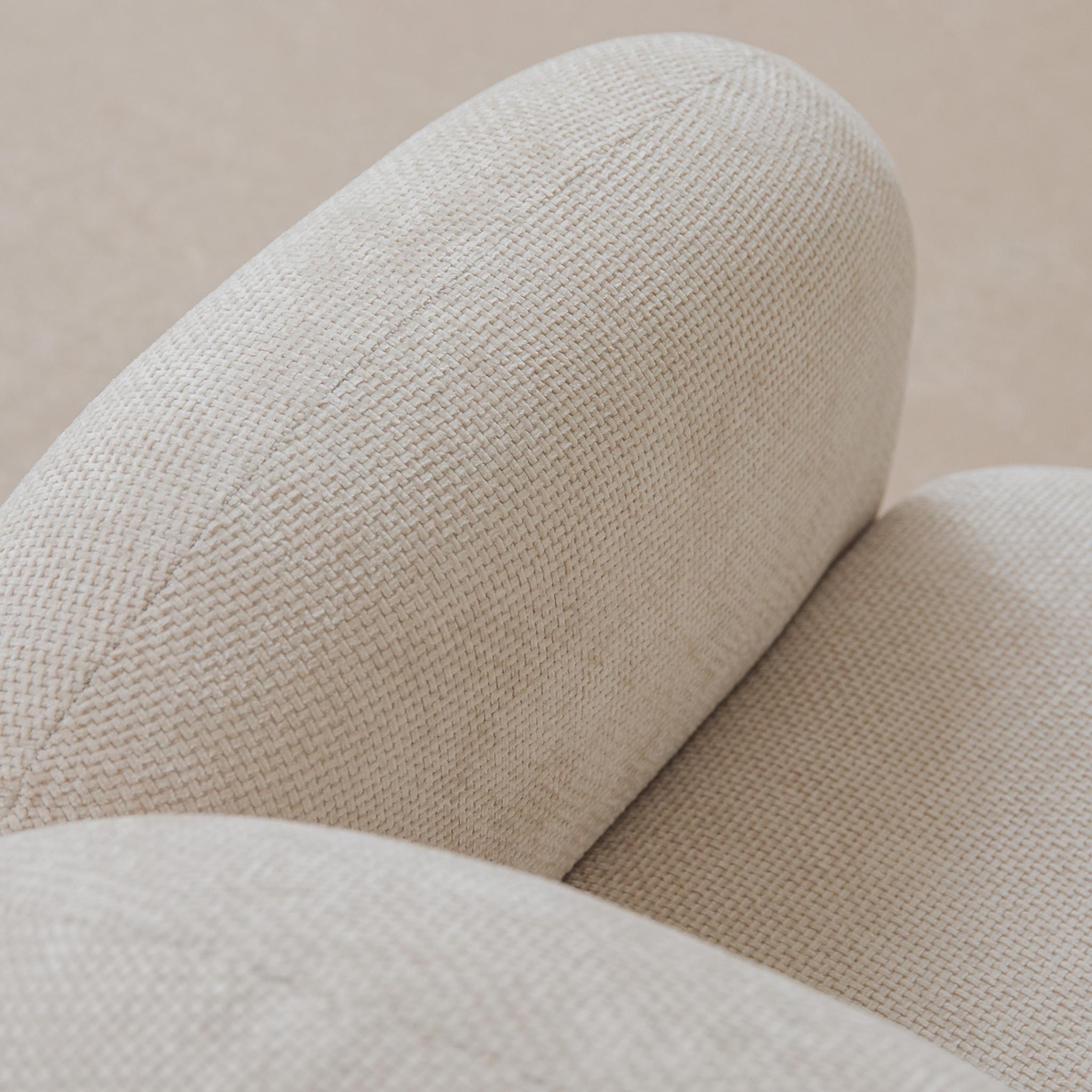 Gros plan sur un canapé Micadoni : accoudoir et dossier arrondis en tissu beige clair à tissage serré.