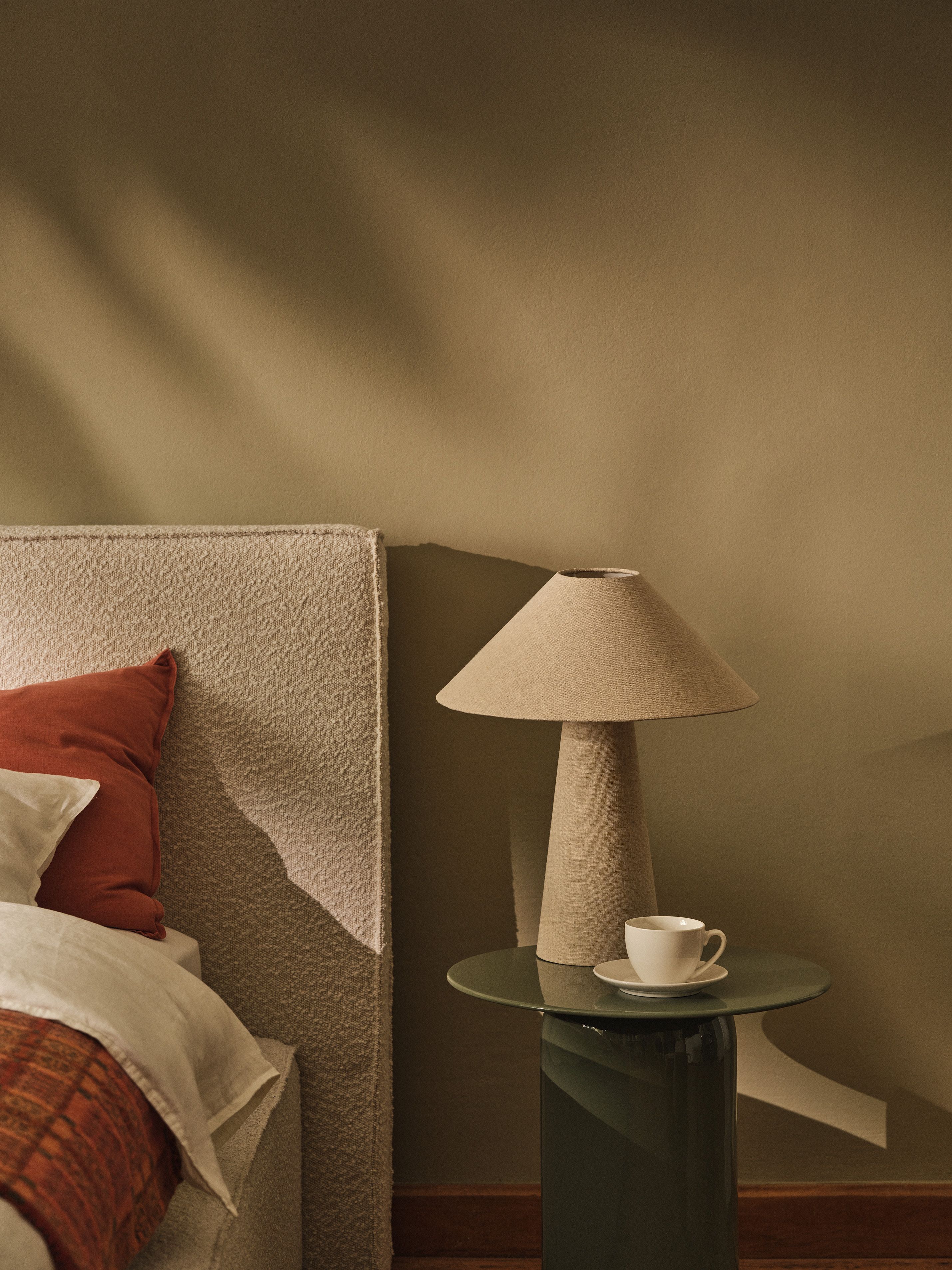 Tête de lit en tissu Micadoni avec lampe de chevet et tasse sur une table d’appoint ronde.