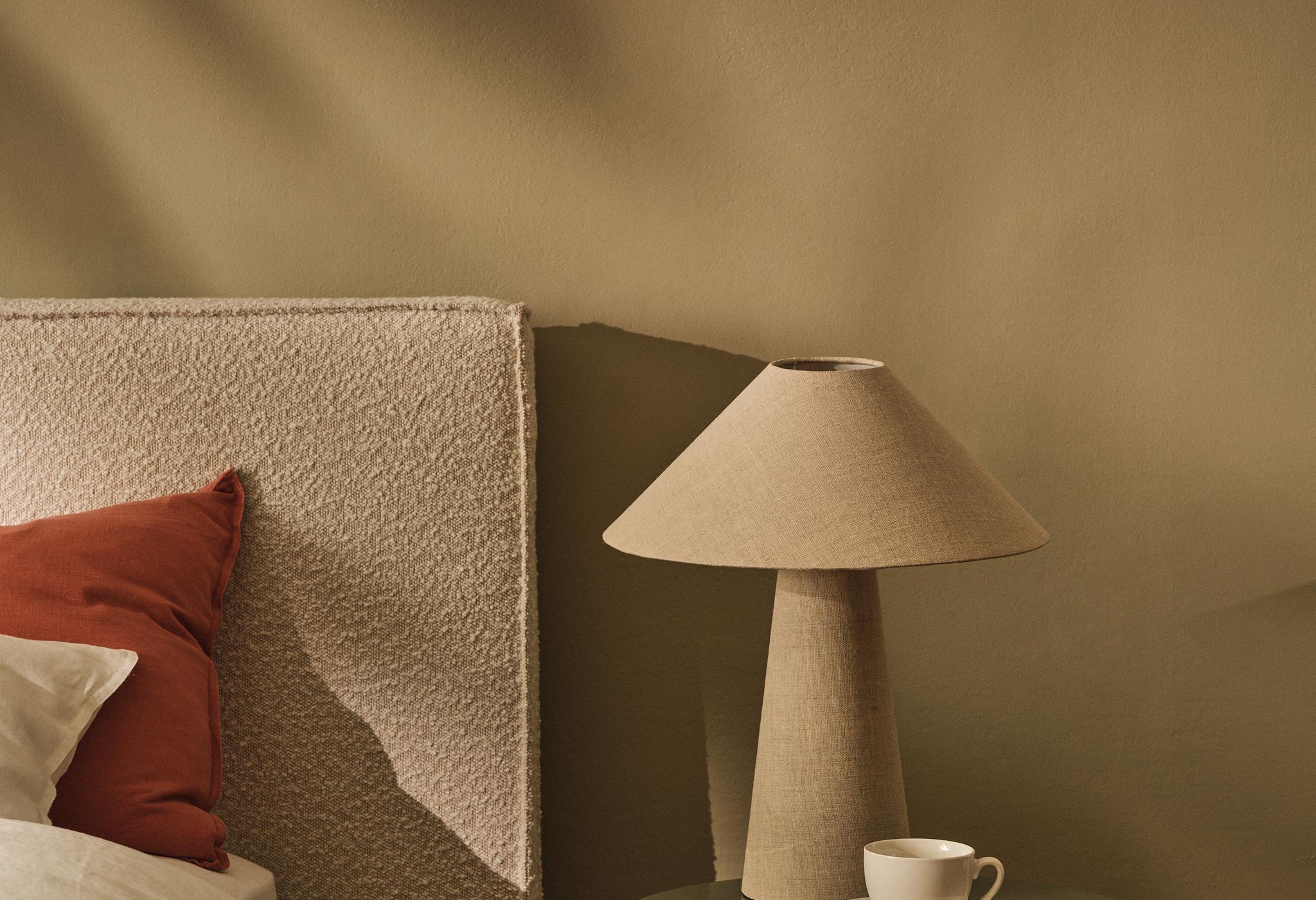 Tête de lit en tissu Micadoni avec lampe de chevet et tasse sur une table d’appoint ronde.