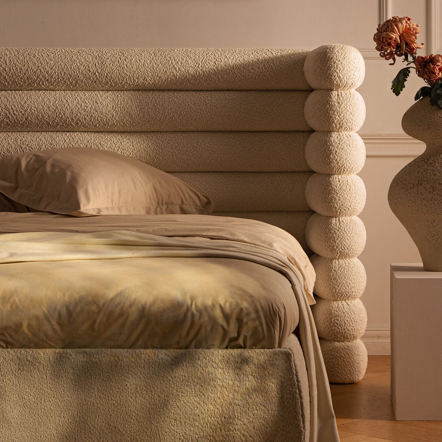 Gros plan sur un lit Micadoni avec tête de lit arrondie capitonnée gris foncé, draps en lin beige et couvre-lit olive.