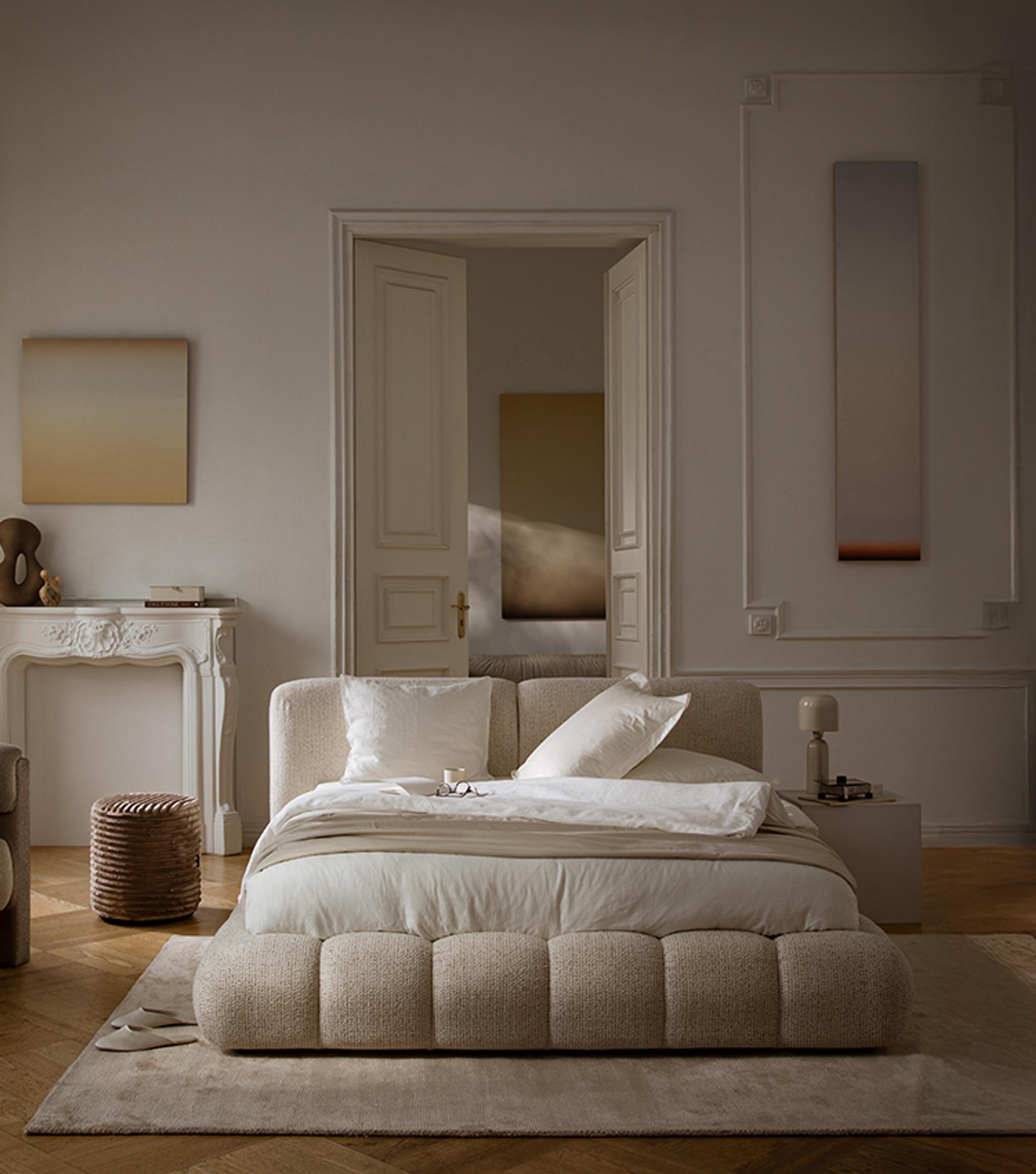 Lit Micadoni Martina avec base capitonnée arrondie et grande tête de lit texturée dans une chambre chaleureuse.