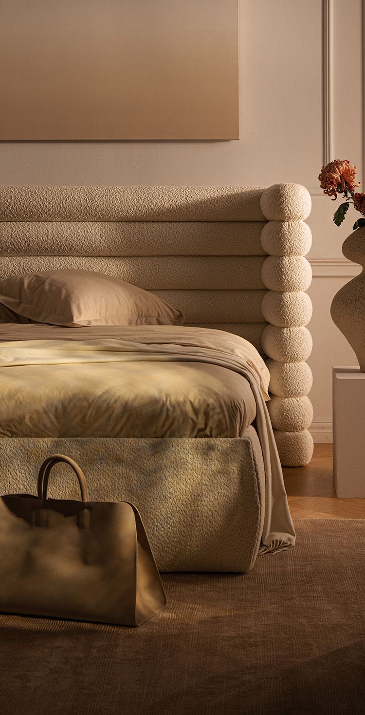 Lit Micadoni Mount avec grande tête de lit à boudins superposés en bouclé crème, paré de linge neutre, posé sur un tapis dans une chambre chaleureuse.