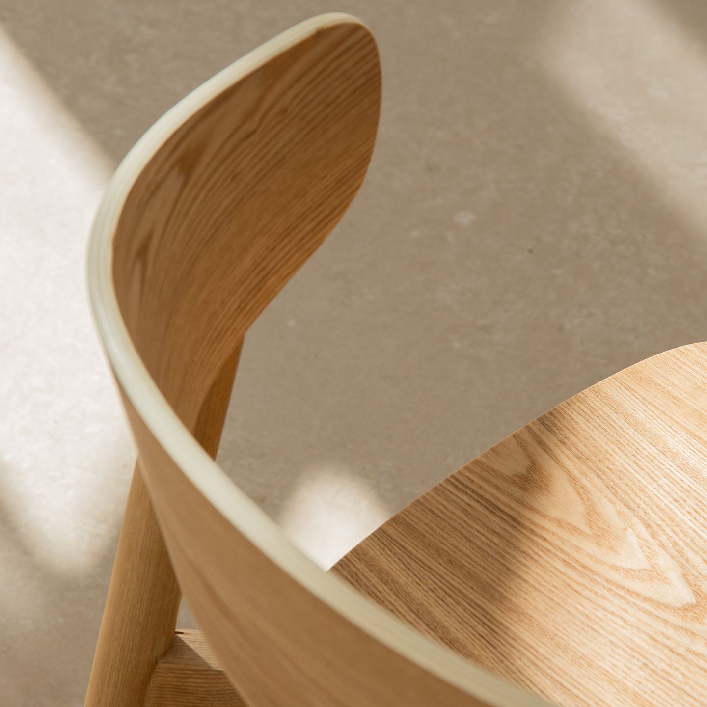 Gros plan d’une chaise de salle à manger Micadoni en bois avec dossier courbé en chêne clair, baignée de lumière.