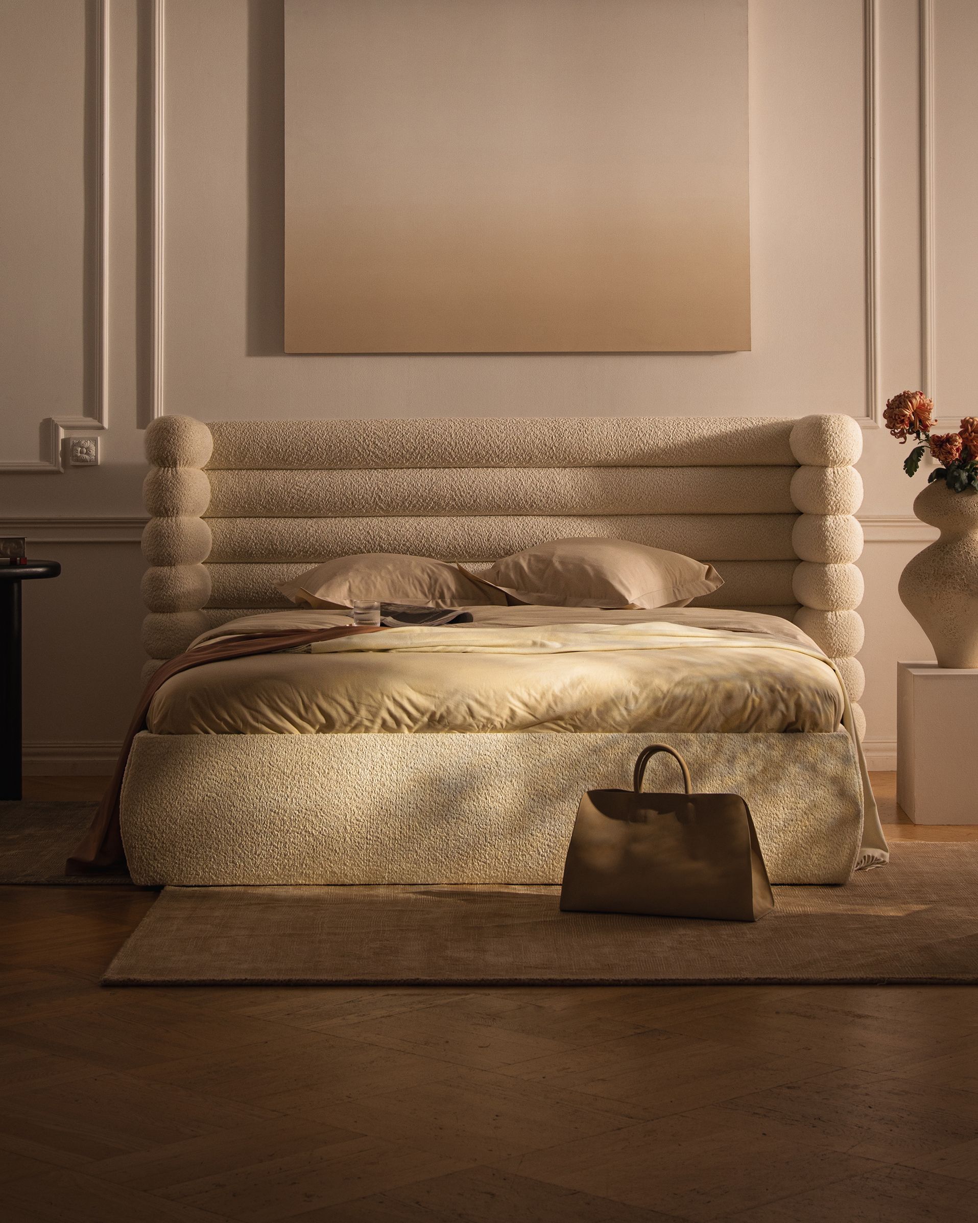 Lit Micadoni Mount avec grande tête de lit à boudins superposés en bouclé crème, paré de linge neutre, posé sur un tapis dans une chambre chaleureuse.