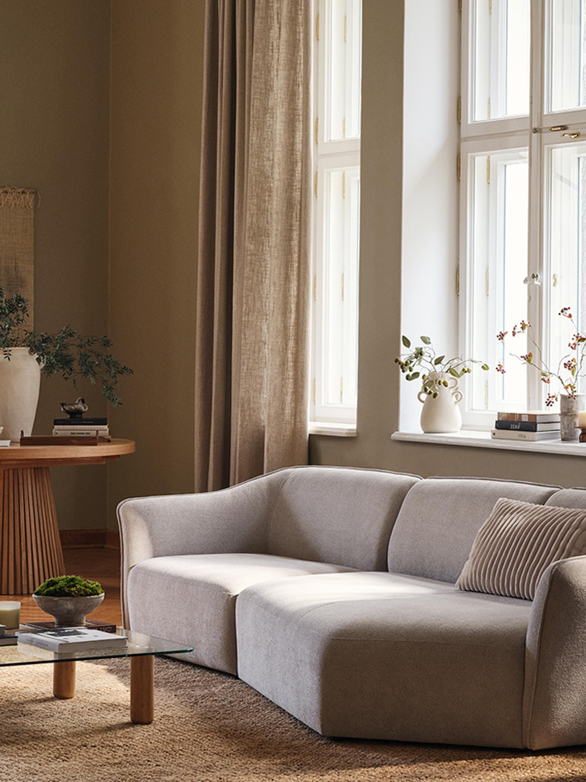 Canapé Hailey de Micadoni avec table basse Moscarte en verre et table à manger ronde Portmany en bois dans un salon chaleureux et ensoleillé