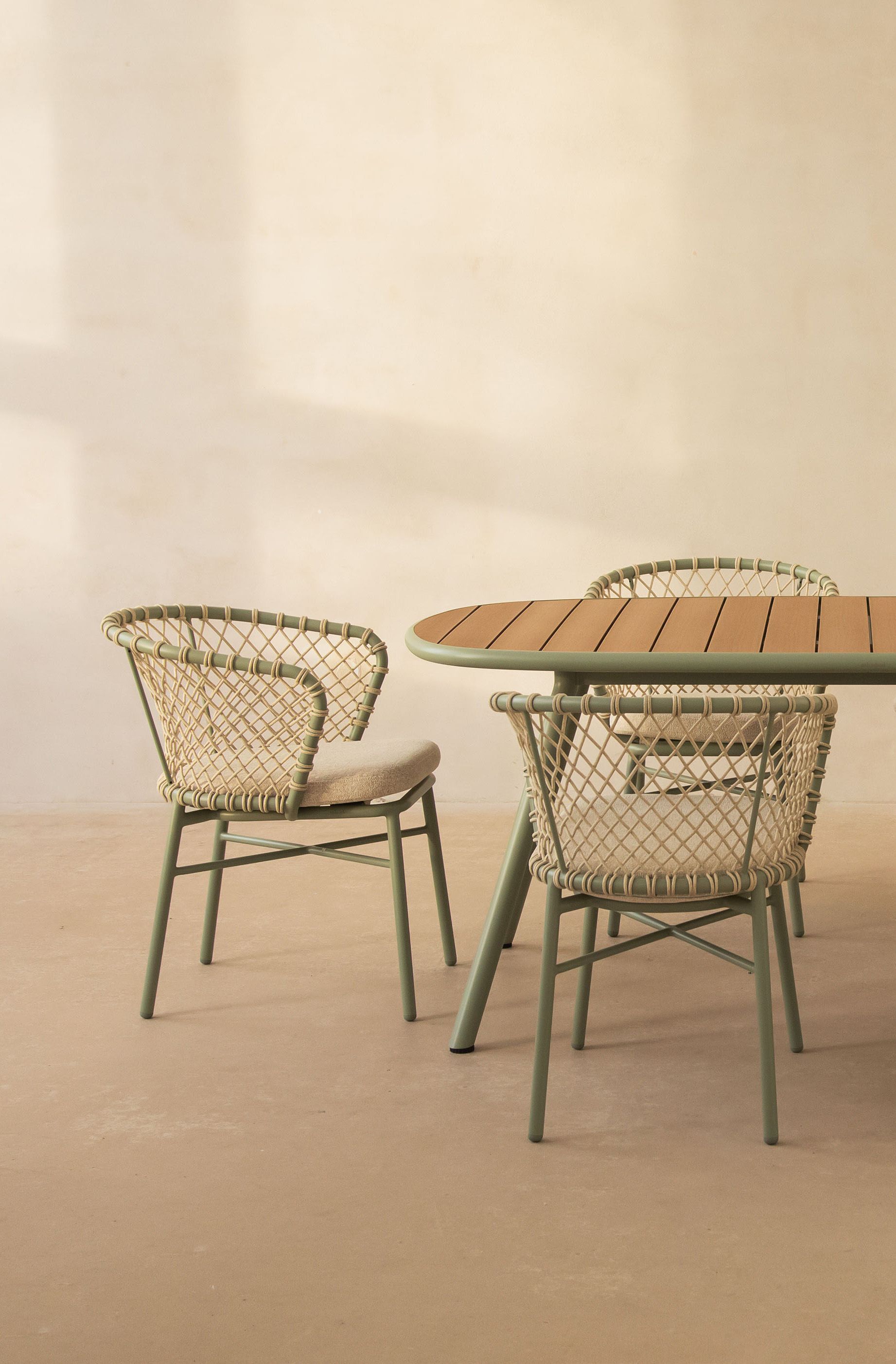 Ensemble d’extérieur Micadoni Margalida avec table ovale à lattes vert sauge et six chaises tressées avec coussins.