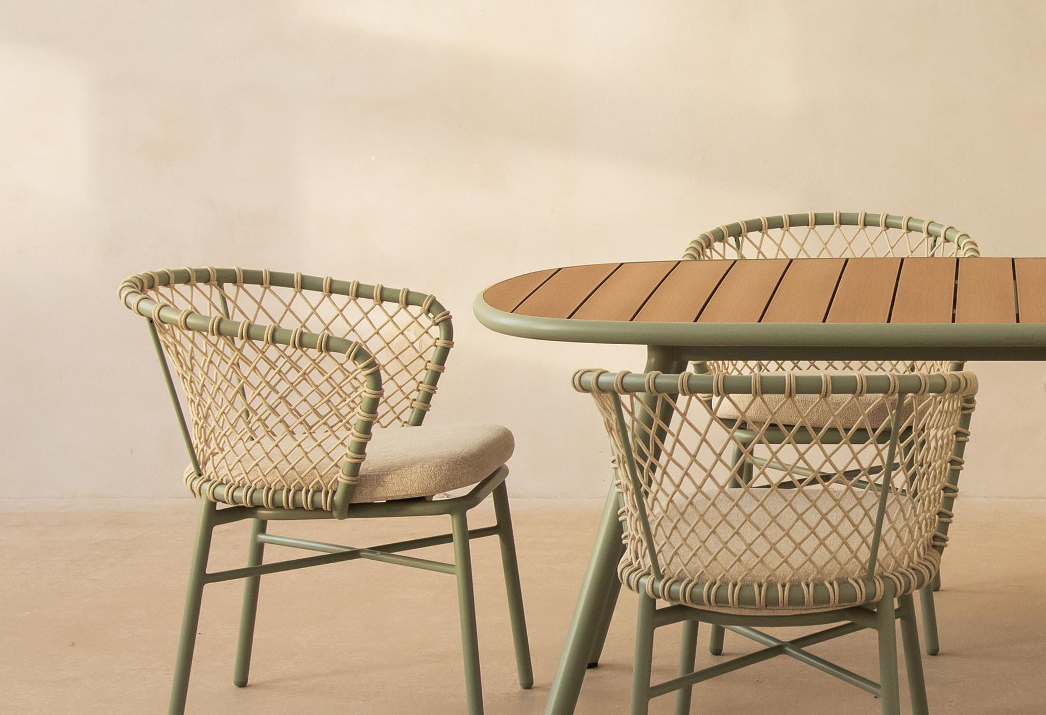 Ensemble d’extérieur Micadoni Margalida avec table ovale à lattes vert sauge et six chaises tressées avec coussins.