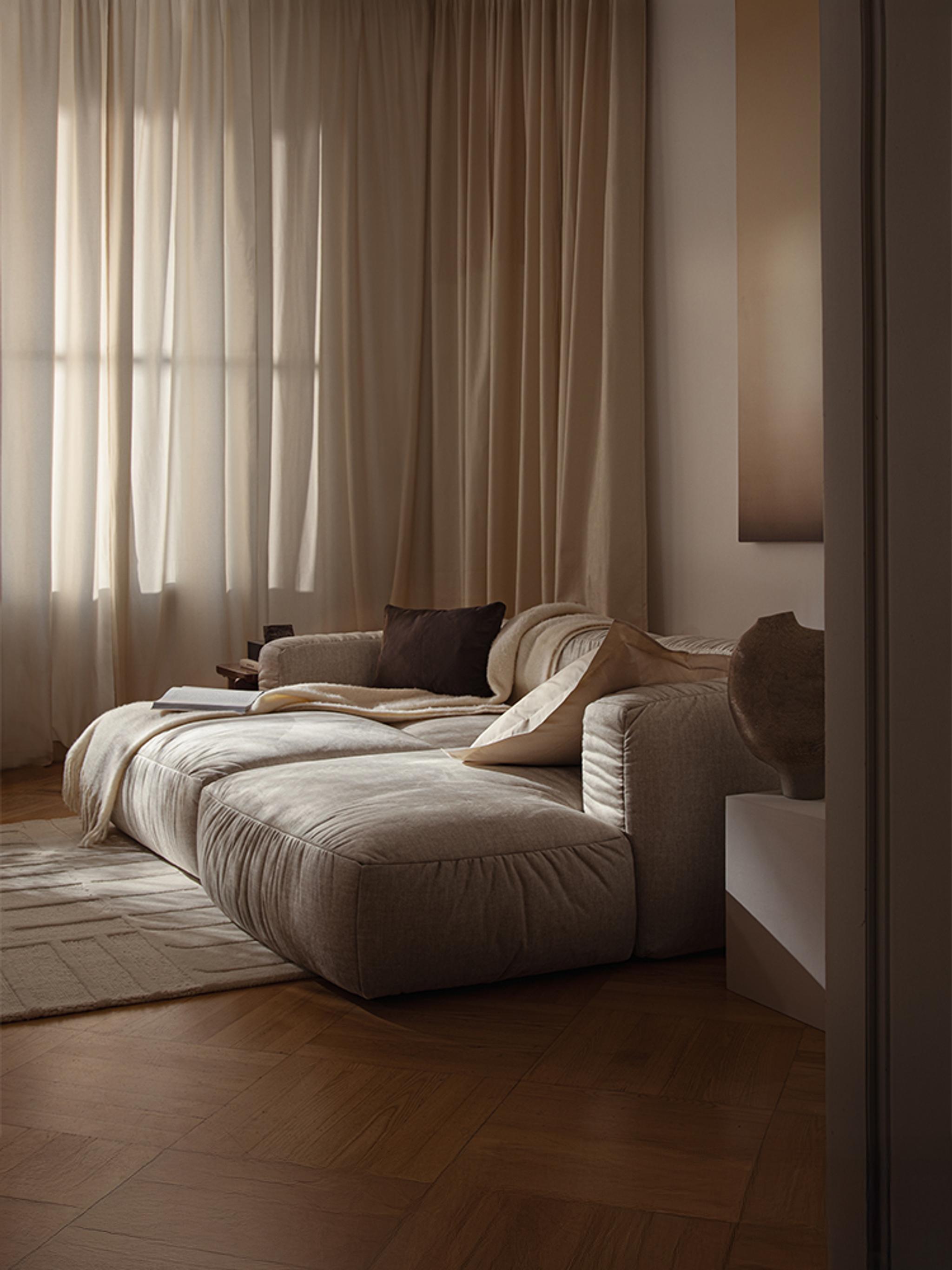 Lit Micadoni Martina en tissu avec tête de lit basse, table d’appoint et linge de lit neutre dans un intérieur classique.