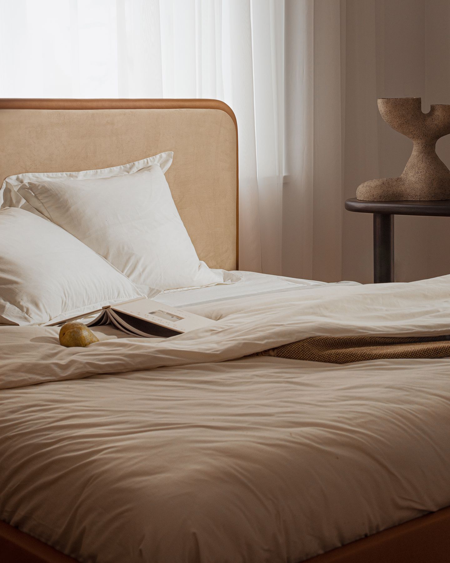 Lit Micadoni avec tête de lit capitonnée et encadrement en bois arrondi, linge de lit blanc, lumière douce.