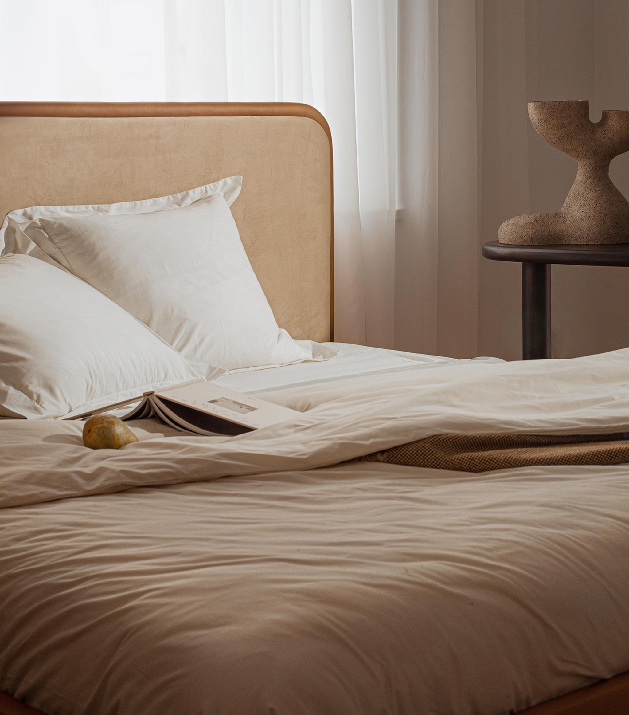 Lit Micadoni avec tête de lit capitonnée et encadrement en bois arrondi, linge de lit blanc, lumière douce.