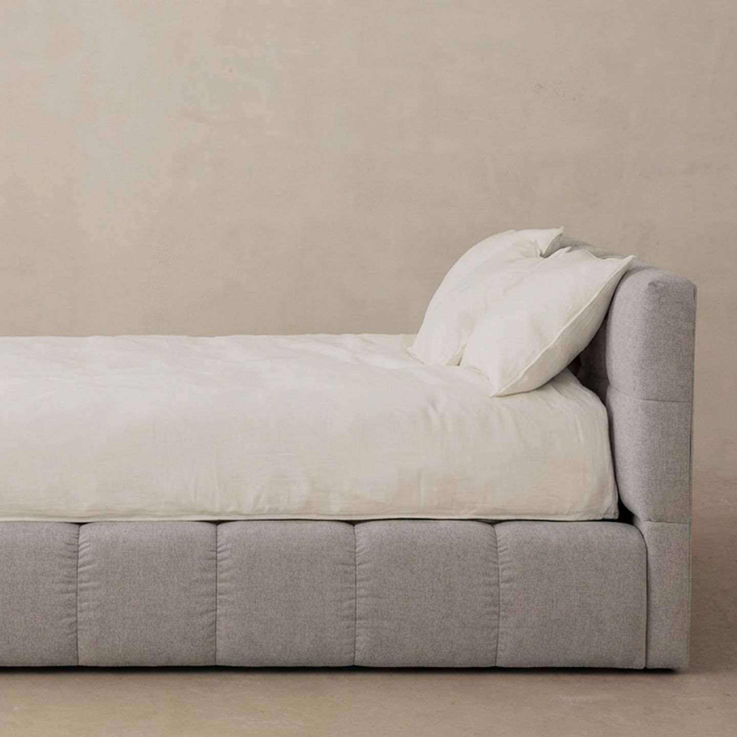 Lit Micadoni tapissé gris clair avec tête de lit rembourrée et base capitonnée, vue latérale, fond studio.