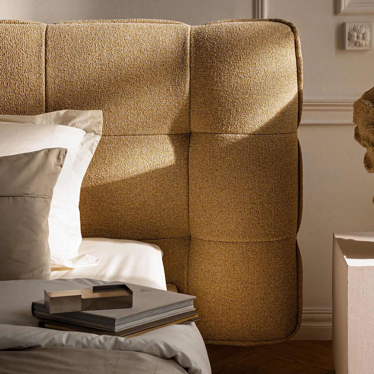 Gros plan sur un lit Micadoni avec tête de lit arrondie capitonnée gris foncé, draps en lin beige et couvre-lit olive.